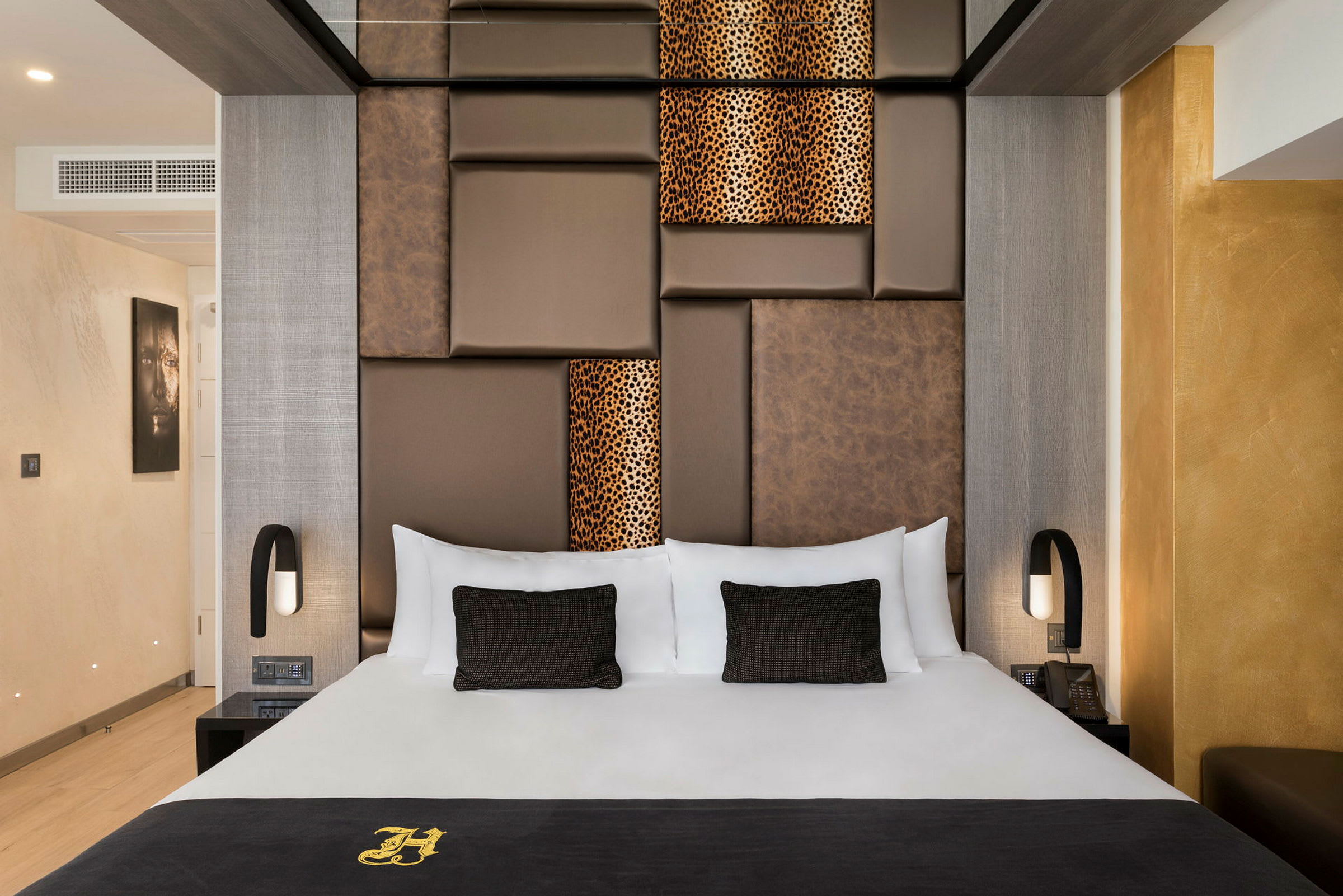 Et elegant hotelværelse med en stor seng, med brune og mønstrede paneler på væggen bagved. Værelset er moderne indrettet med varme farver. (AI-genereret tekst)