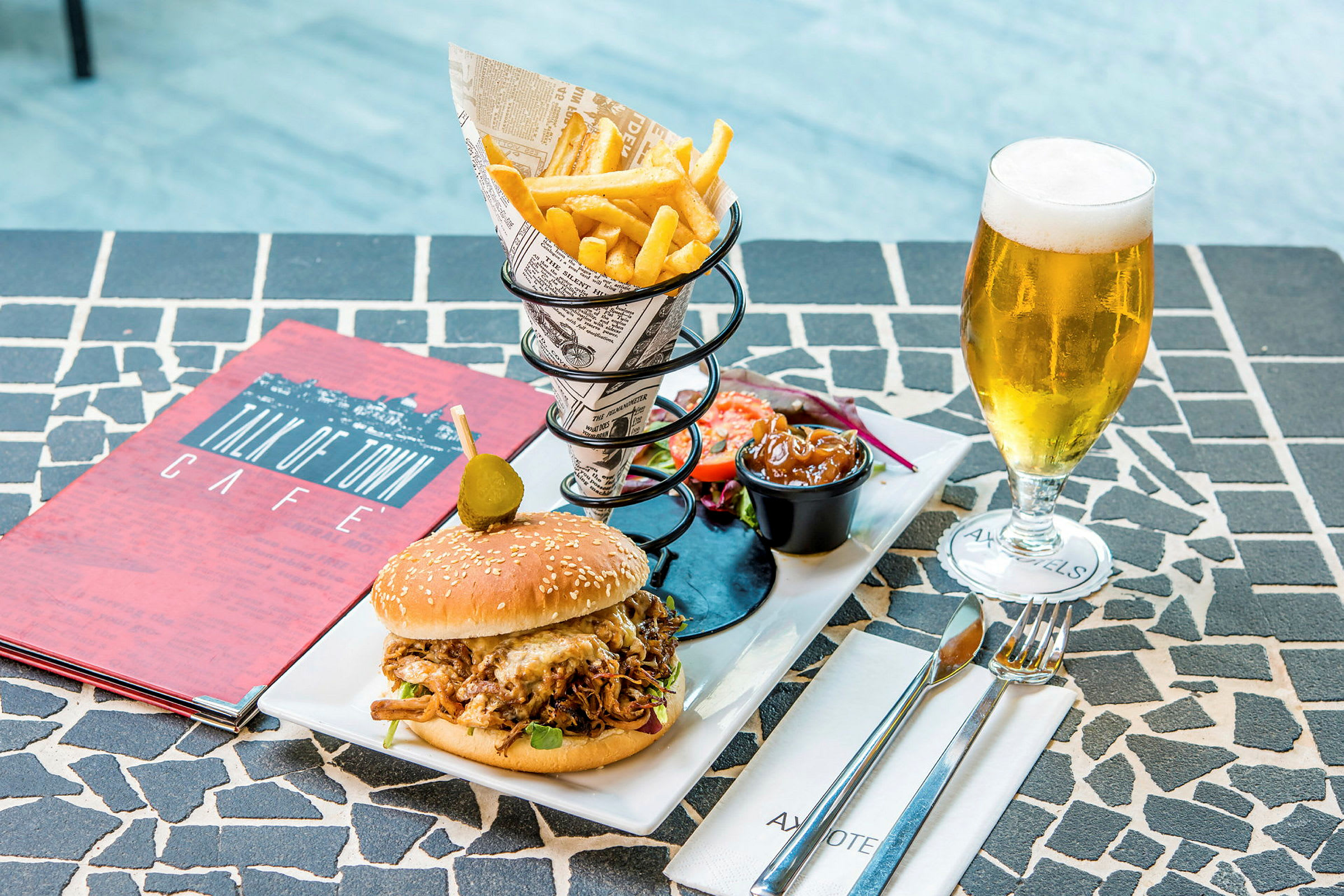 En tallerken med en burger, pommes frites, salat, sauce og et glas øl på et bord. (AI-genereret tekst)