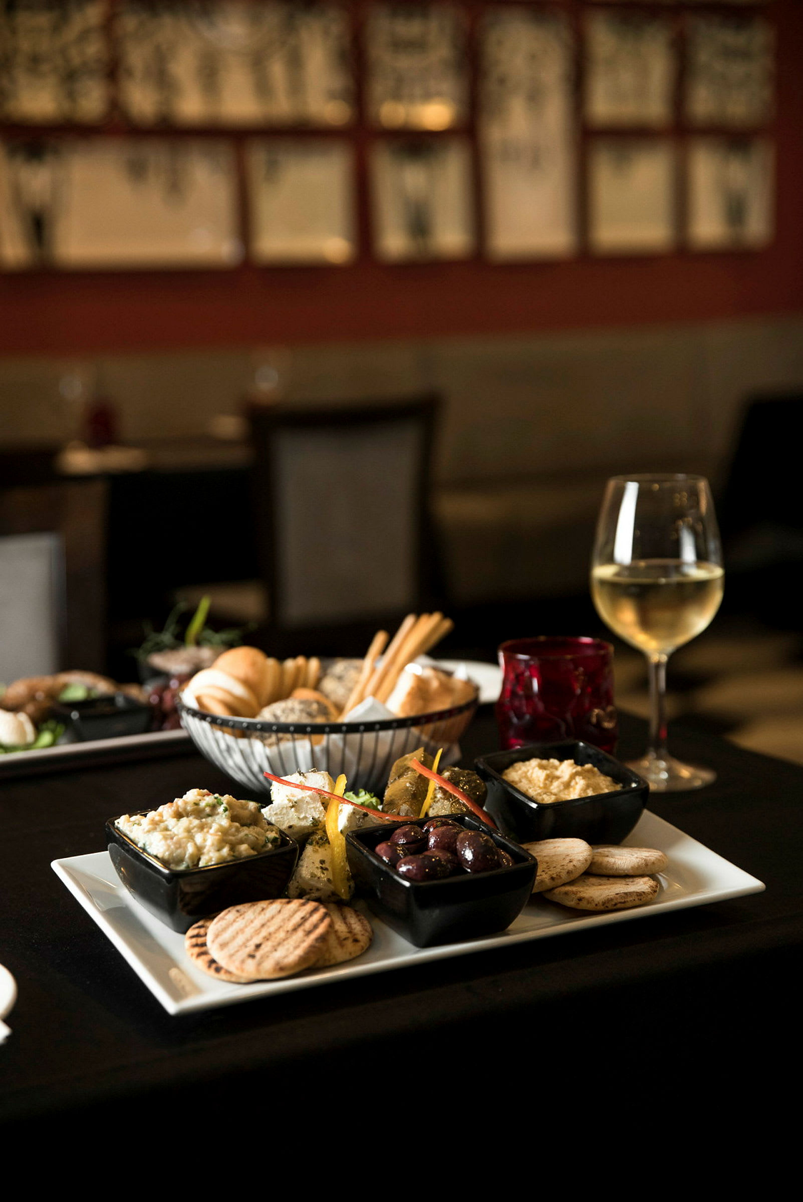 En tallerken med forskellige småretter, inklusive oliven, hummus og brød, serveres sammen med et glas hvidvin. (AI-genereret tekst)
