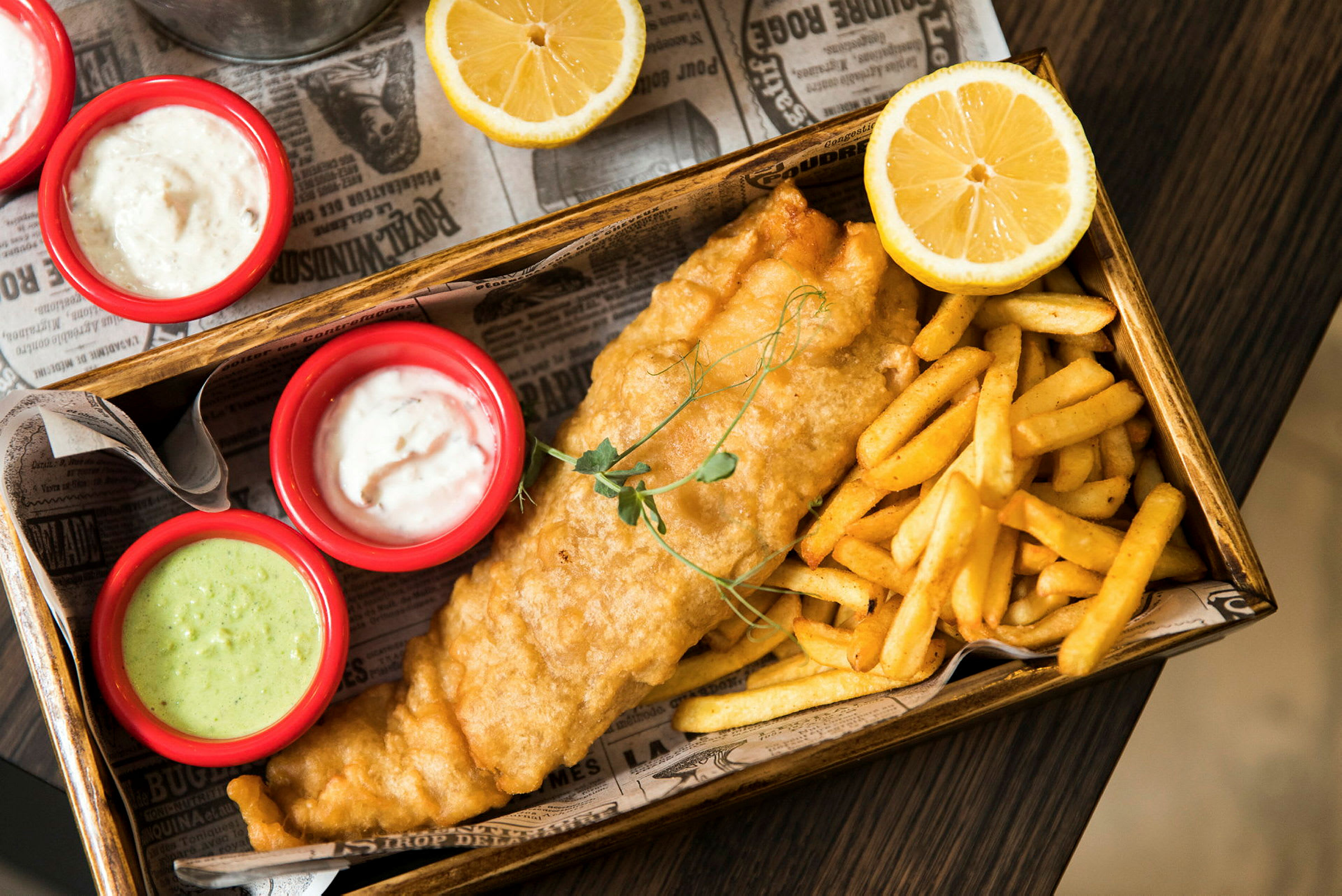 Fish and chips serveret med saucer og citronhalvdele. (AI-genereret tekst)