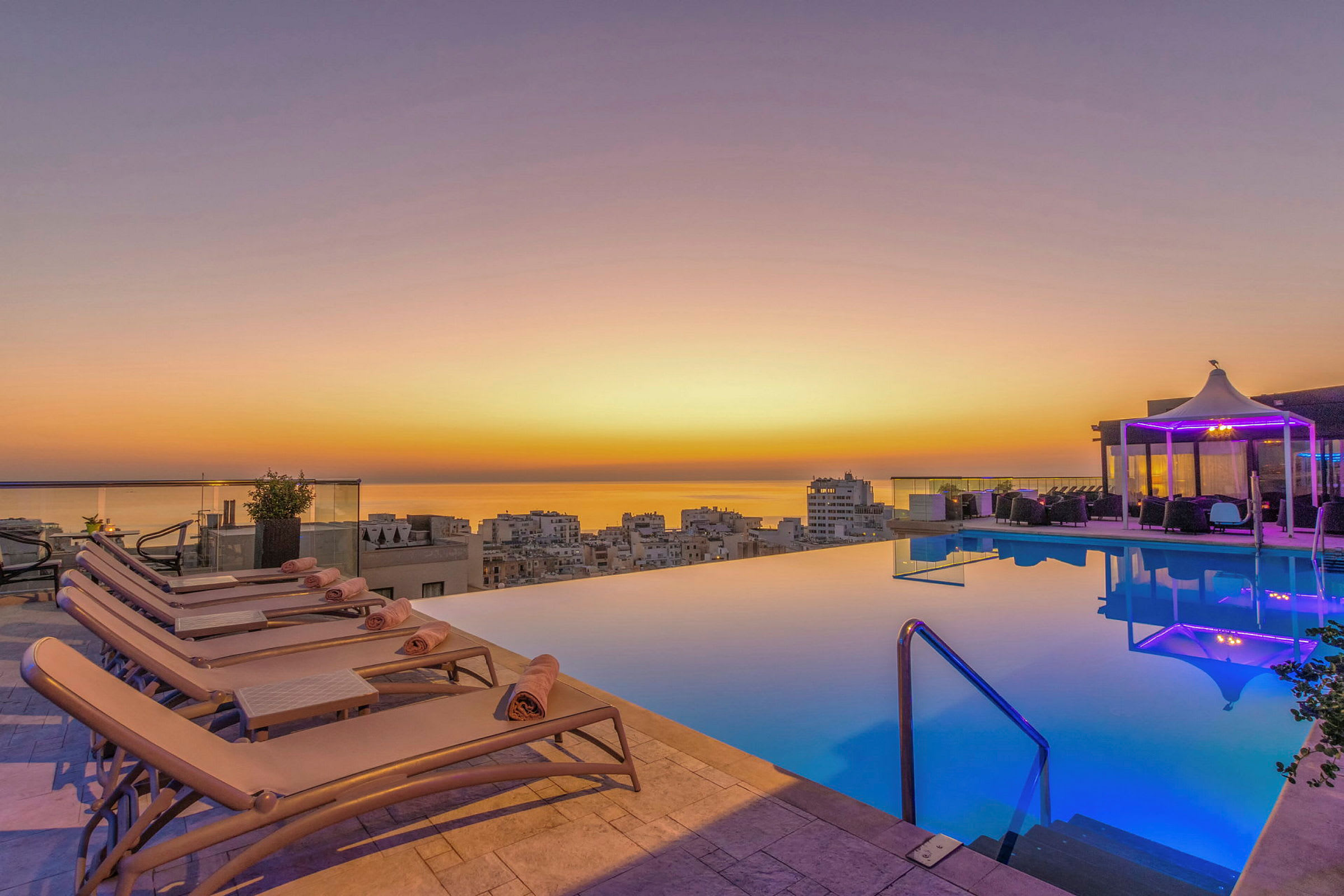 En infinitypool ved solnedgang, med liggestole og en pavillon i baggrunden. (AI-genereret tekst)