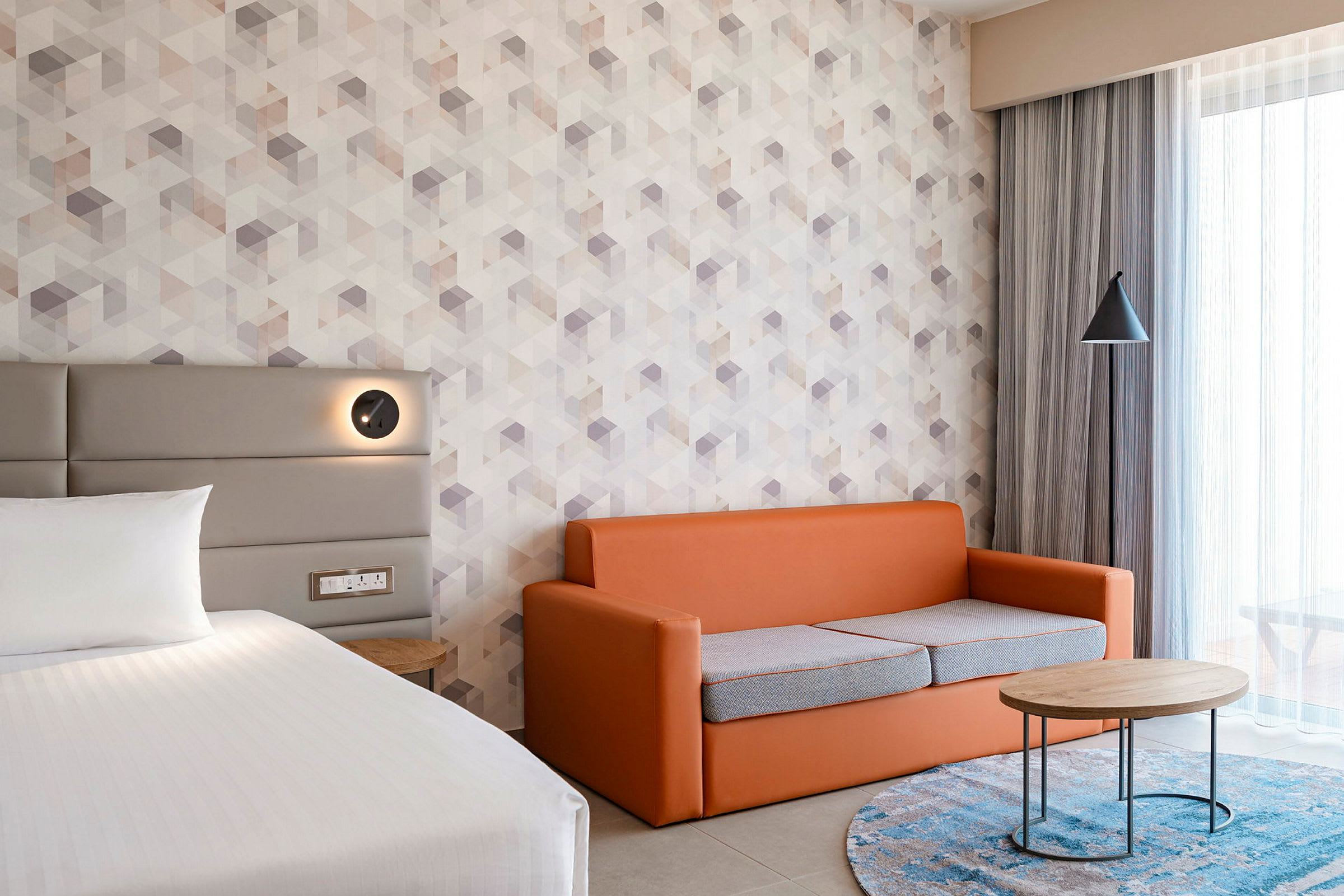 Et hotelværelse med en seng, en orange sofa og et rundt sofabord. (AI-genereret tekst)