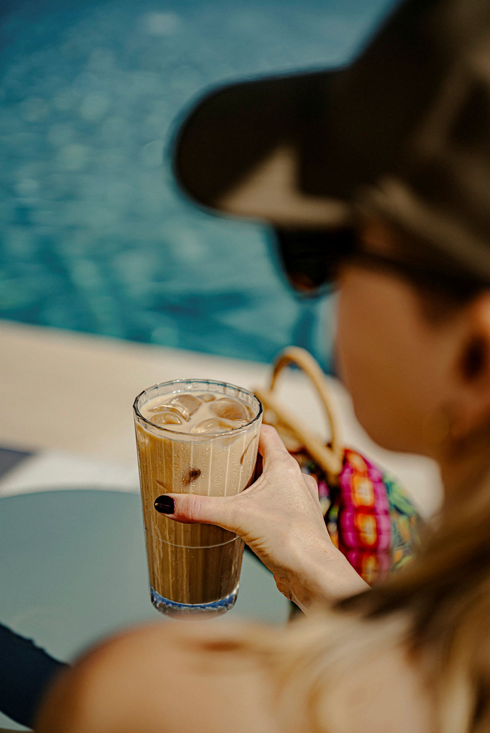 Et glas iskaffe bliver holdt ved en pool. (AI-genereret tekst)