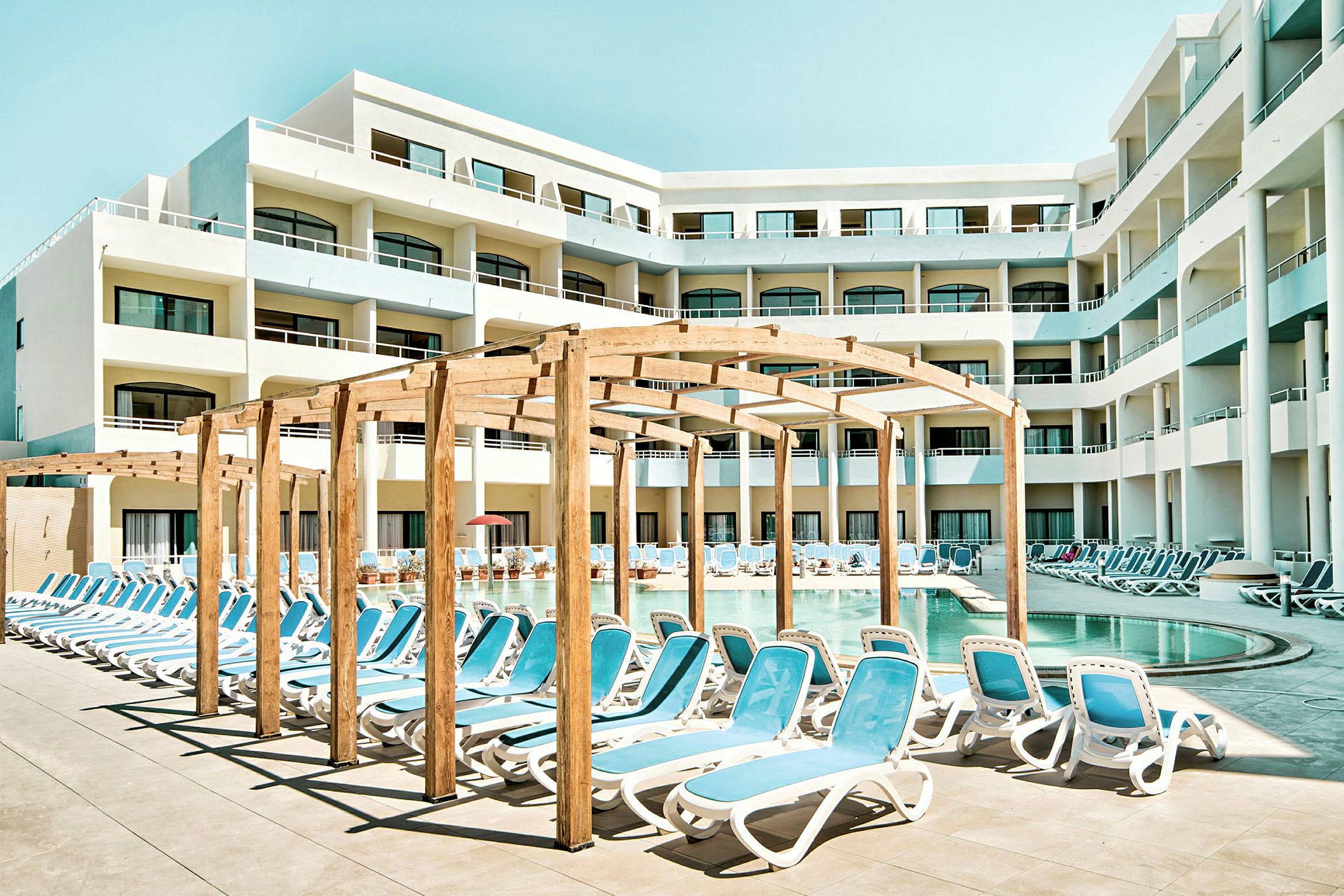 Poolområde ved hotel med liggestole og skyggefuld pergola. (AI-genereret tekst)