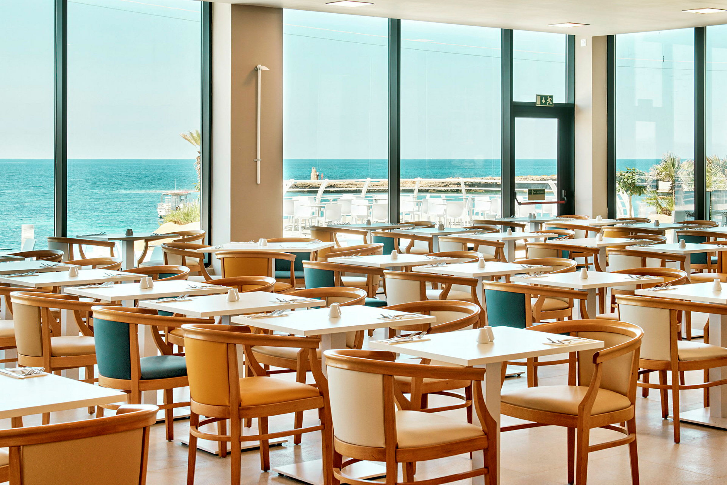 Restaurant med flere borde og stole, stor vindudsigt til havet. (AI-genereret tekst)
