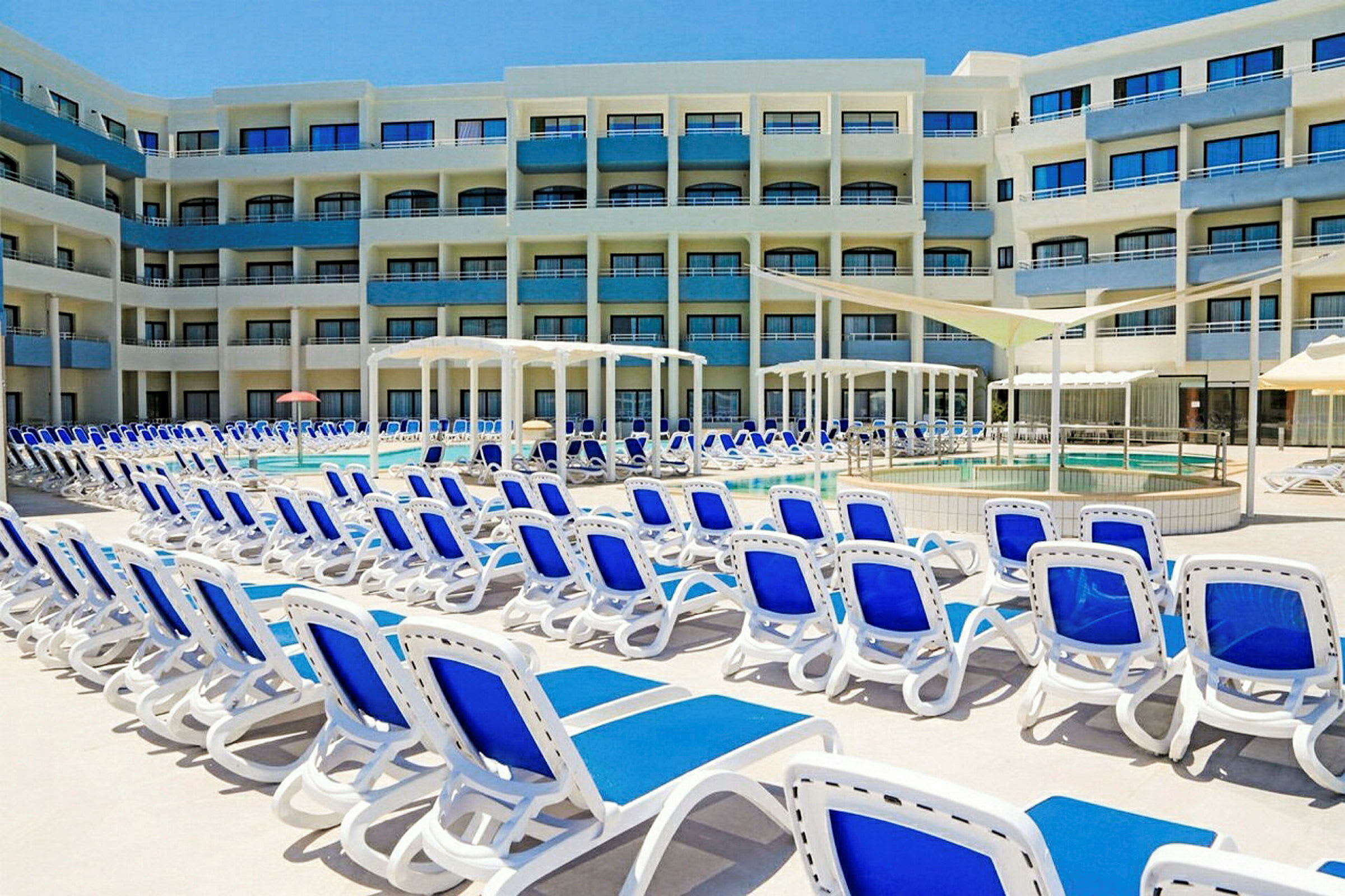 Et hotel med blå og hvide solsenge omkring en udendørs pool. (AI-genereret tekst)