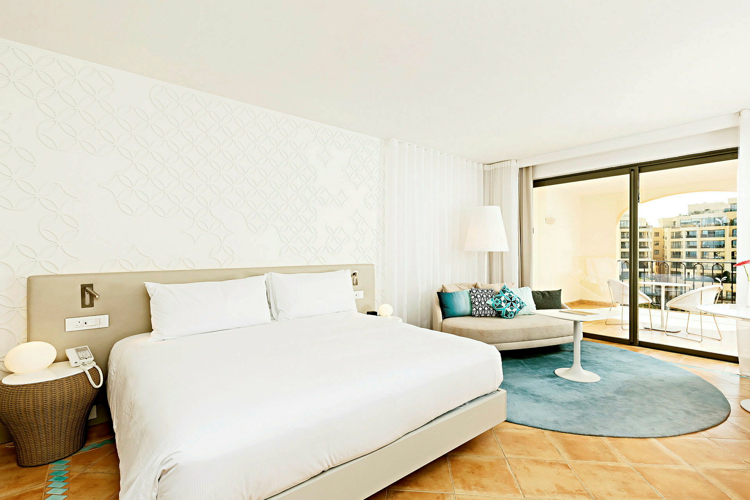 Et moderne hotelværelse med en stor seng, lyse vægge og elegant indretning. Værelset har et siddeområde med puder samt en rummelig balkon med udsigt. (AI-genereret tekst)