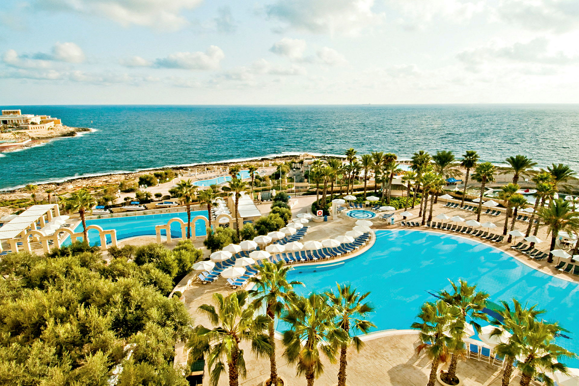 Billede af en resort ved havet med pools, parasoller og palmer. (AI-genereret tekst)