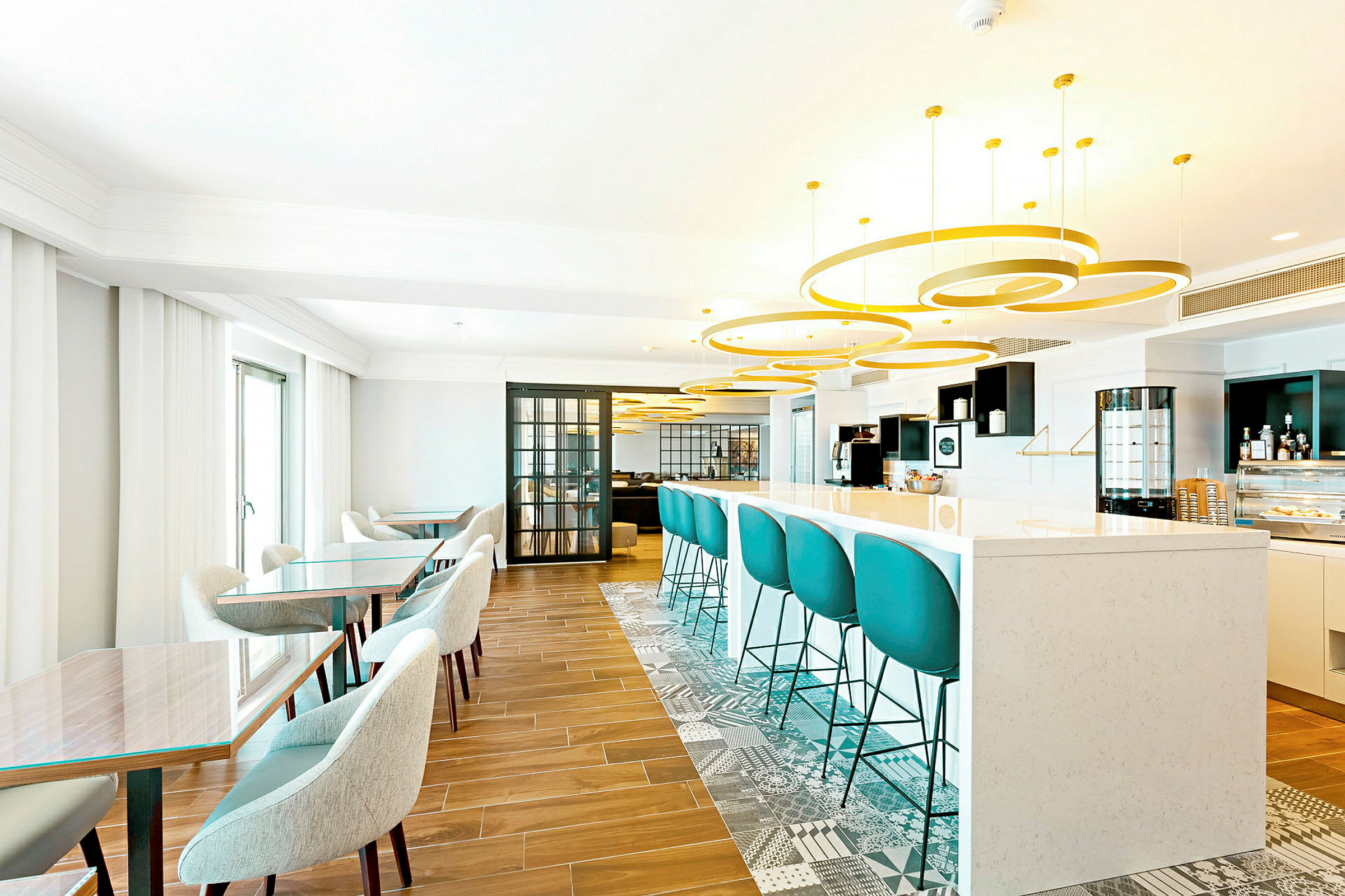En lys og moderne lounge med stole og borde samt en bardisk med turkisfarvede barstole. (AI-genereret tekst)