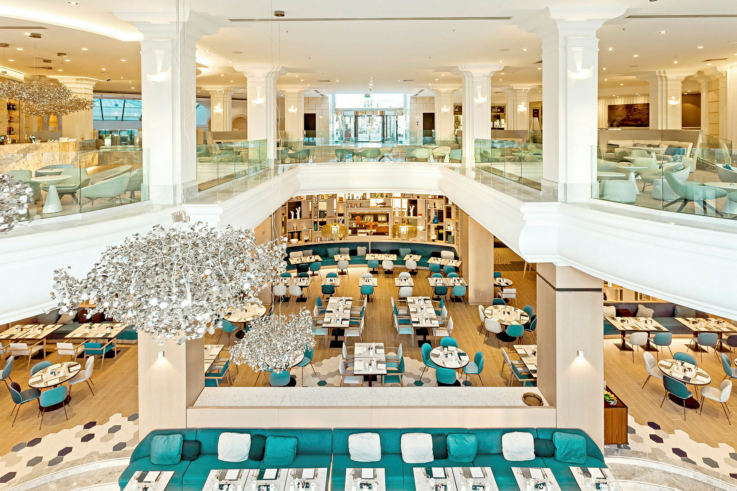 Interiør af en moderne restaurant med åben planløsning, lyse møbler og dekorative lysekroner. (AI-genereret tekst)