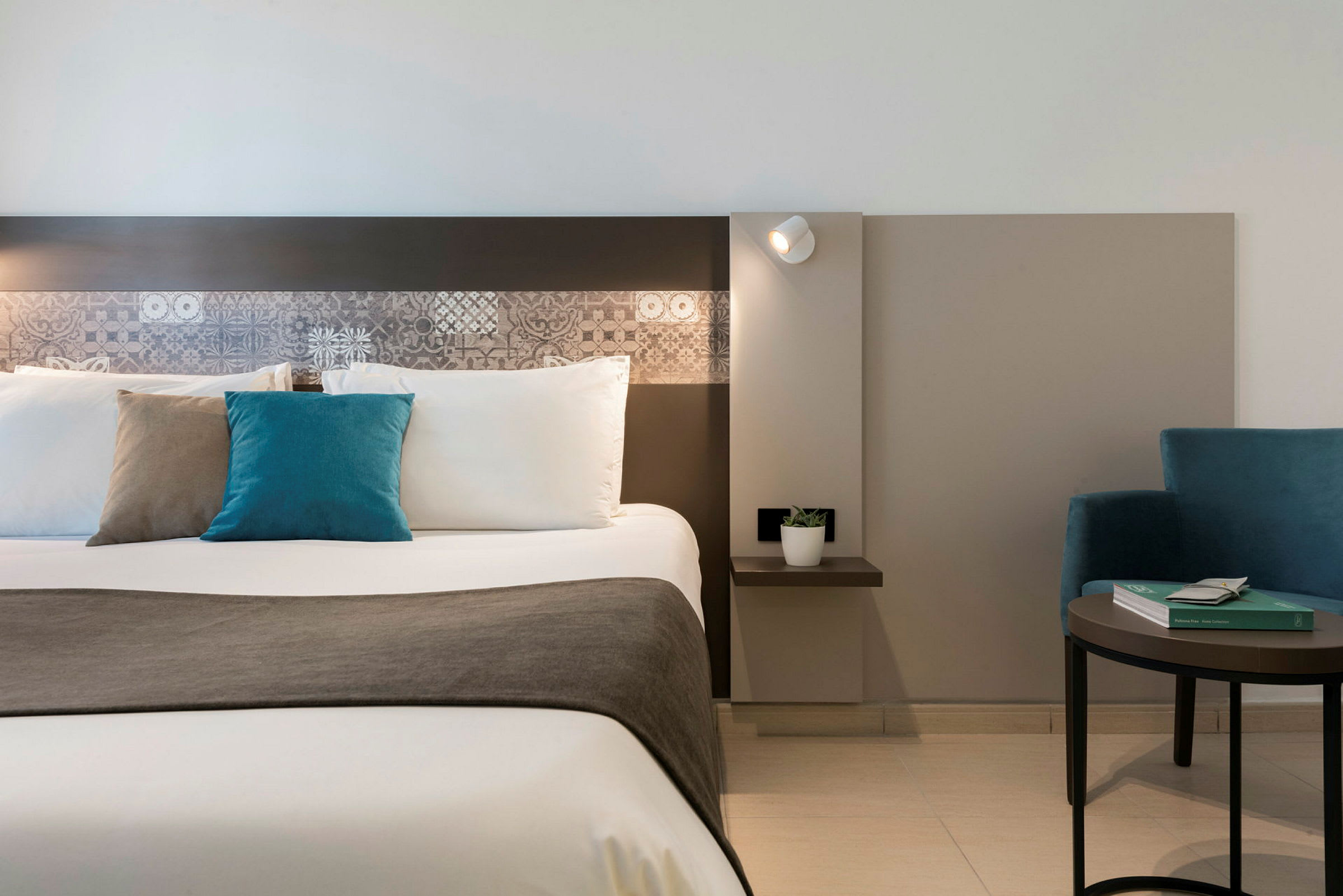 Billede der viser moderne indretning i et hotelværelse med en redt seng og en blå lænestol. (AI-genereret tekst)