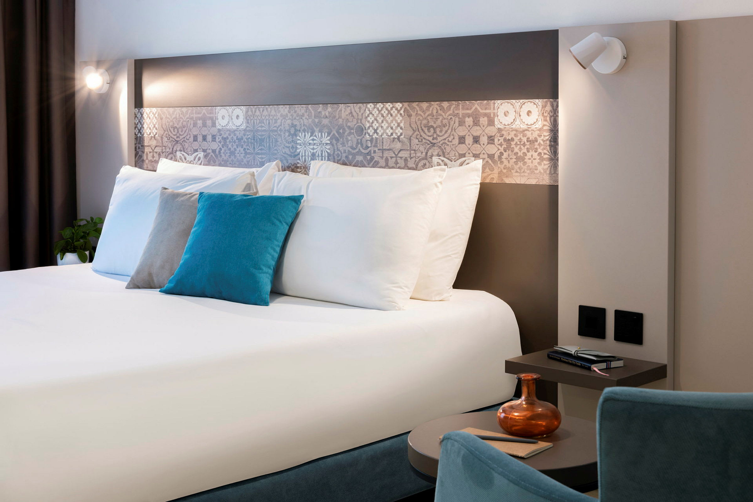 Et moderne hotelværelse med en dobbeltseng, dekorative puder, et natbord og belysning. (AI-genereret tekst)