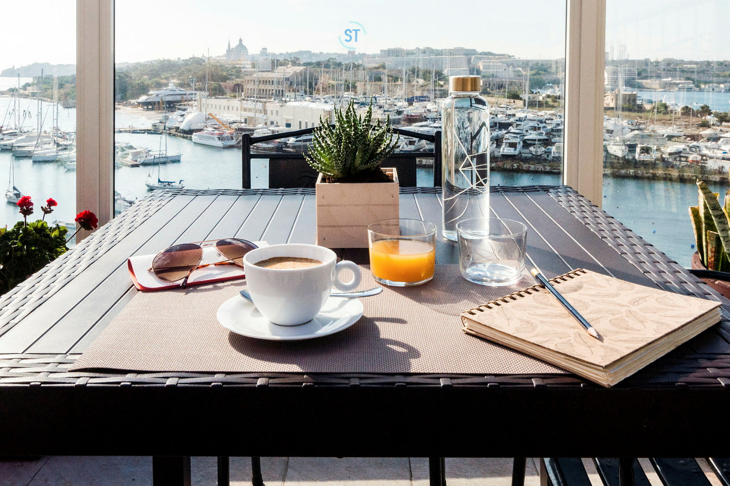 Morgenmadsbord placeret på en terrasse med udsigt over en marina. (AI-genereret tekst)