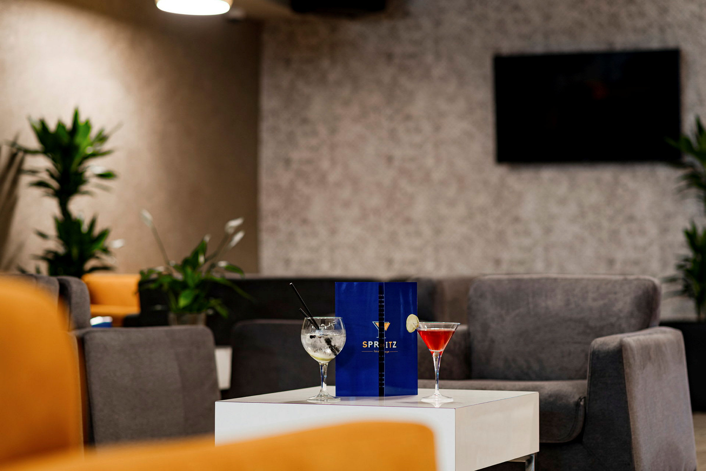 Et bord i en moderne lounge omgivet af komfortable siddepladser, med to cocktailglas og en menu placeret ovenpå. (AI-genereret tekst)