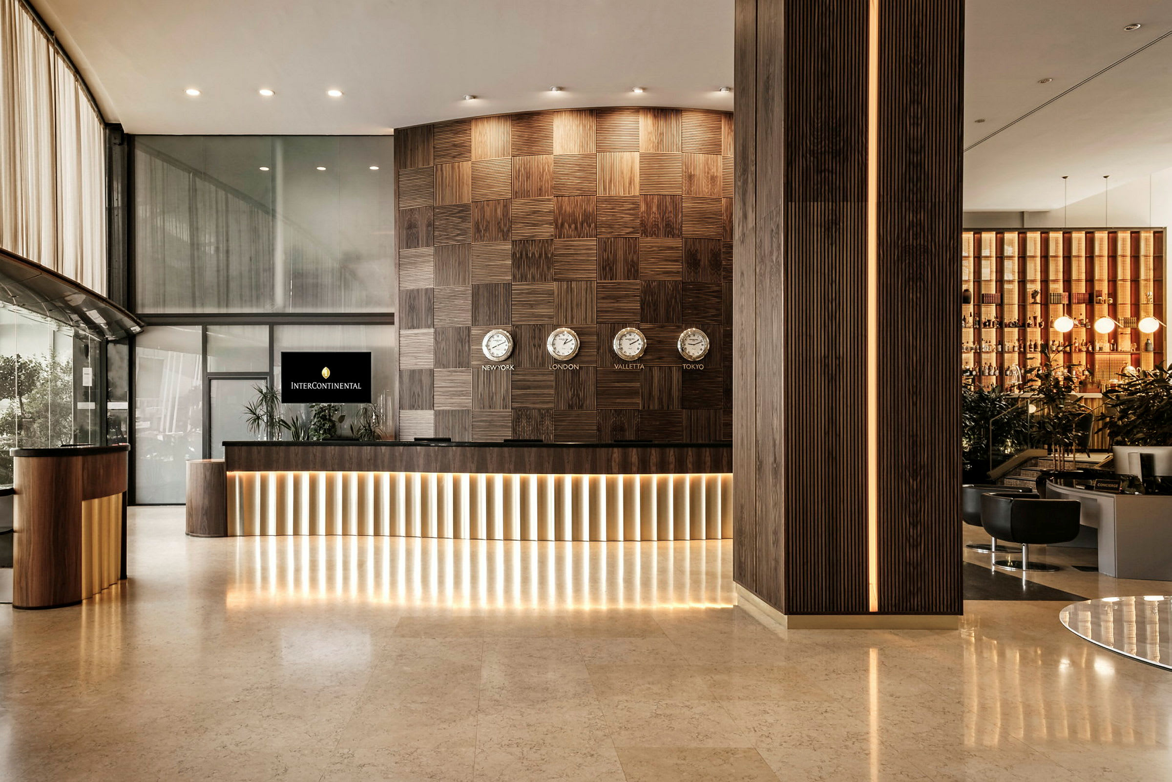 Receptionen på et hotel med moderne design, mørke træpaneler og flere ure, der viser forskellige tidszoner. (AI-genereret tekst)