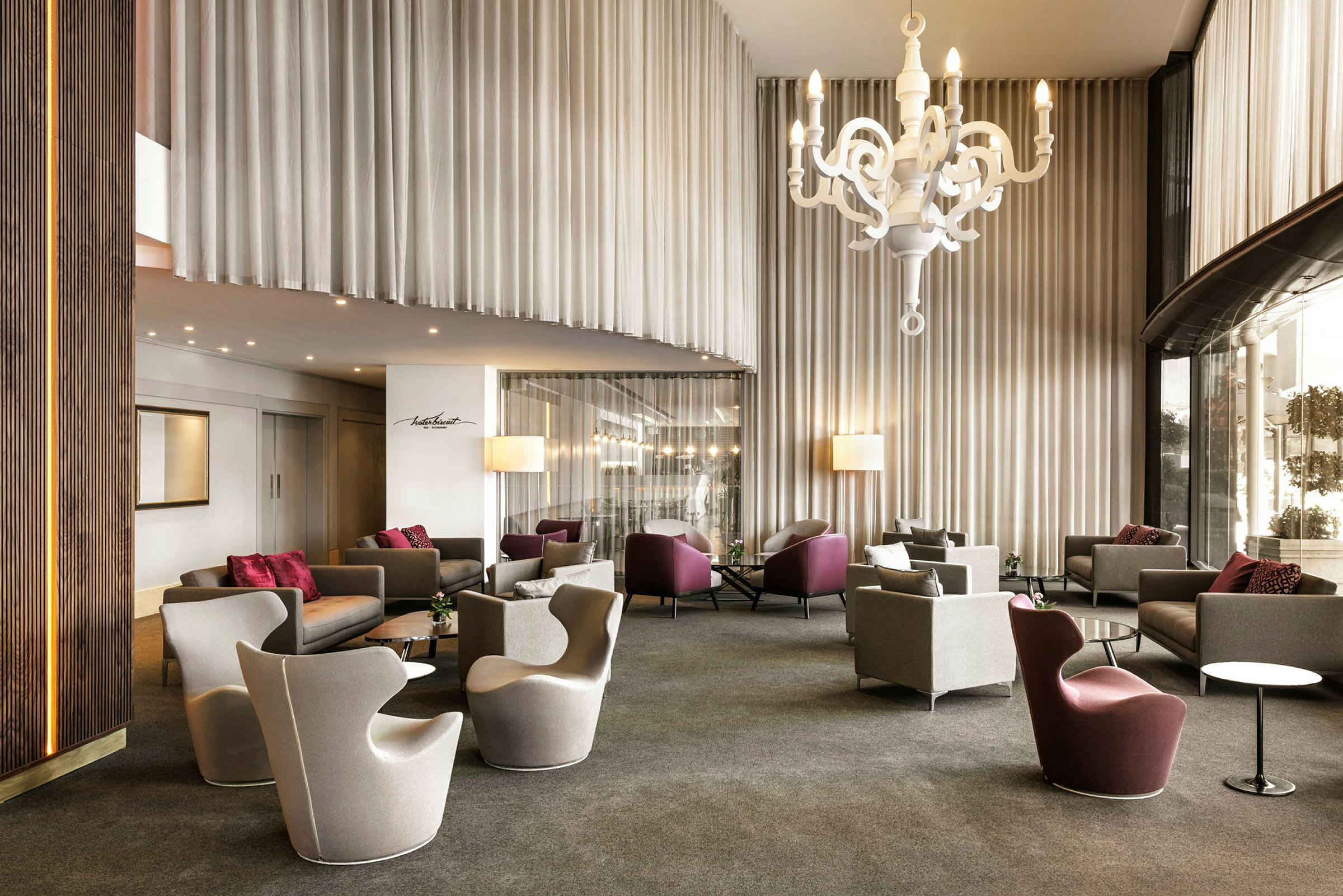 En hotellobby med moderne stole og sofaer, en stor hvid loftlysekrone og høje gardiner. (AI-genereret tekst)
