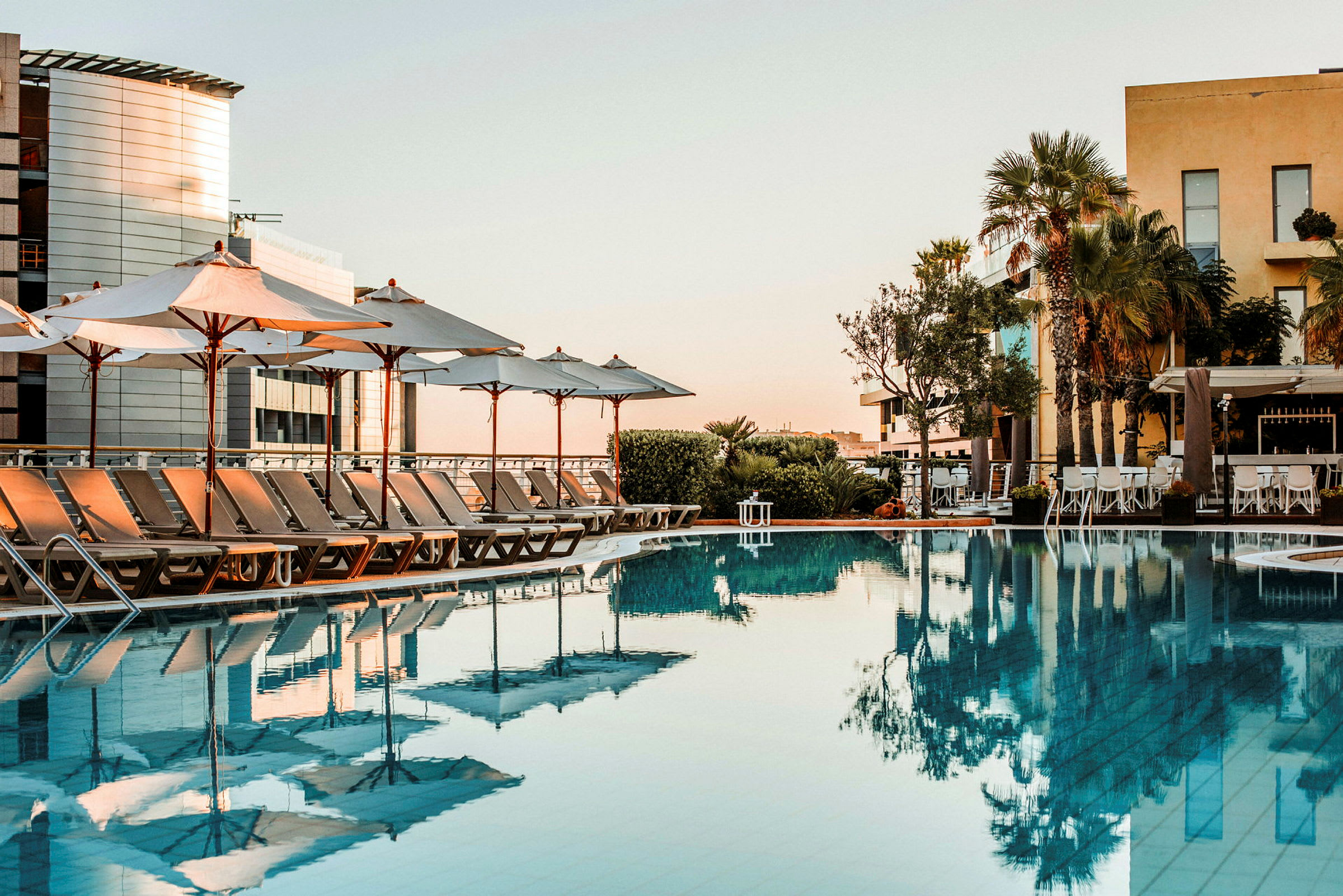 Billede af en udendørs swimmingpool med liggestole og parasoller omkring. (AI-genereret tekst)