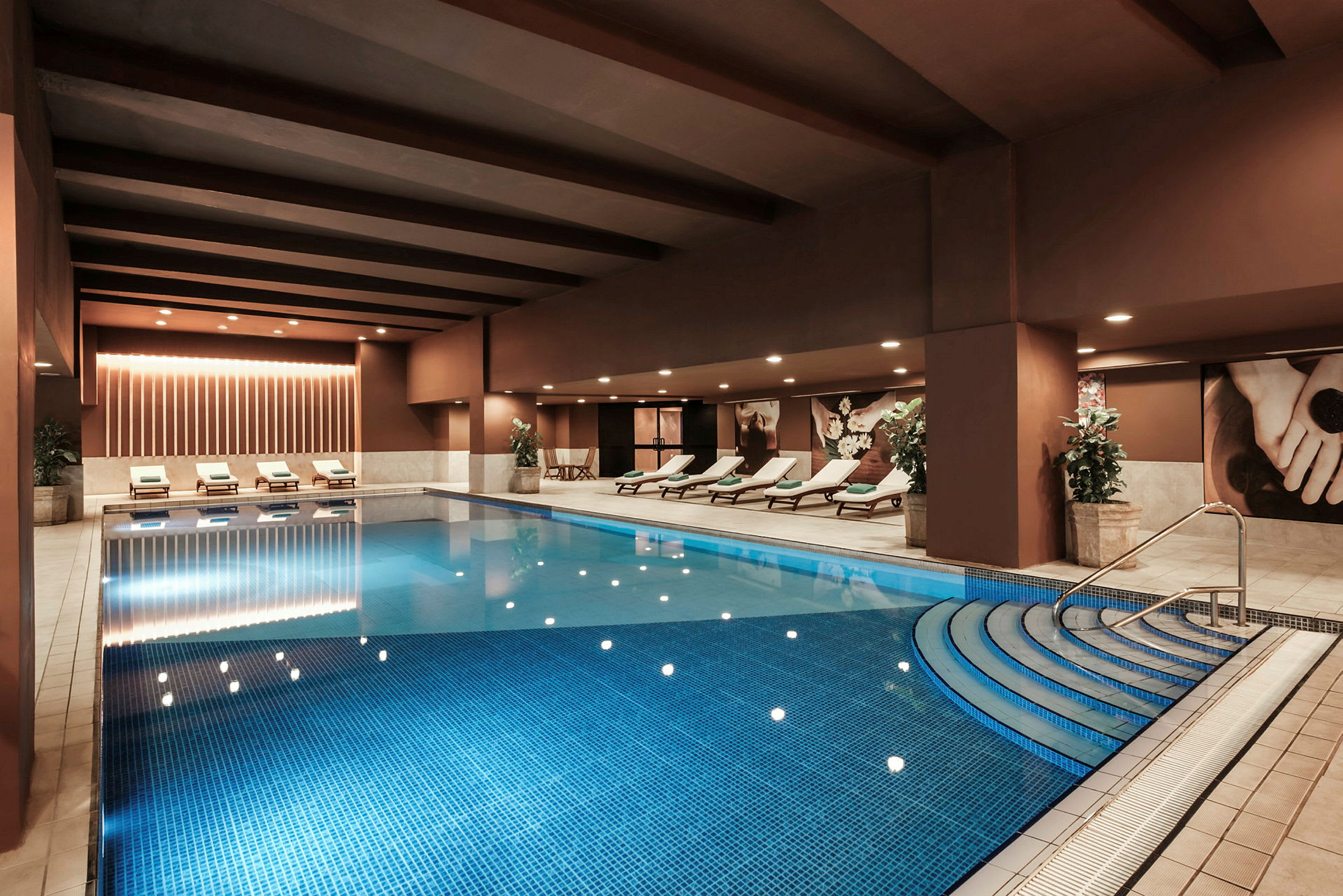 En rummelig indendørs swimmingpool med liggestole og dekorative planter langs siderne. (AI-genereret tekst)