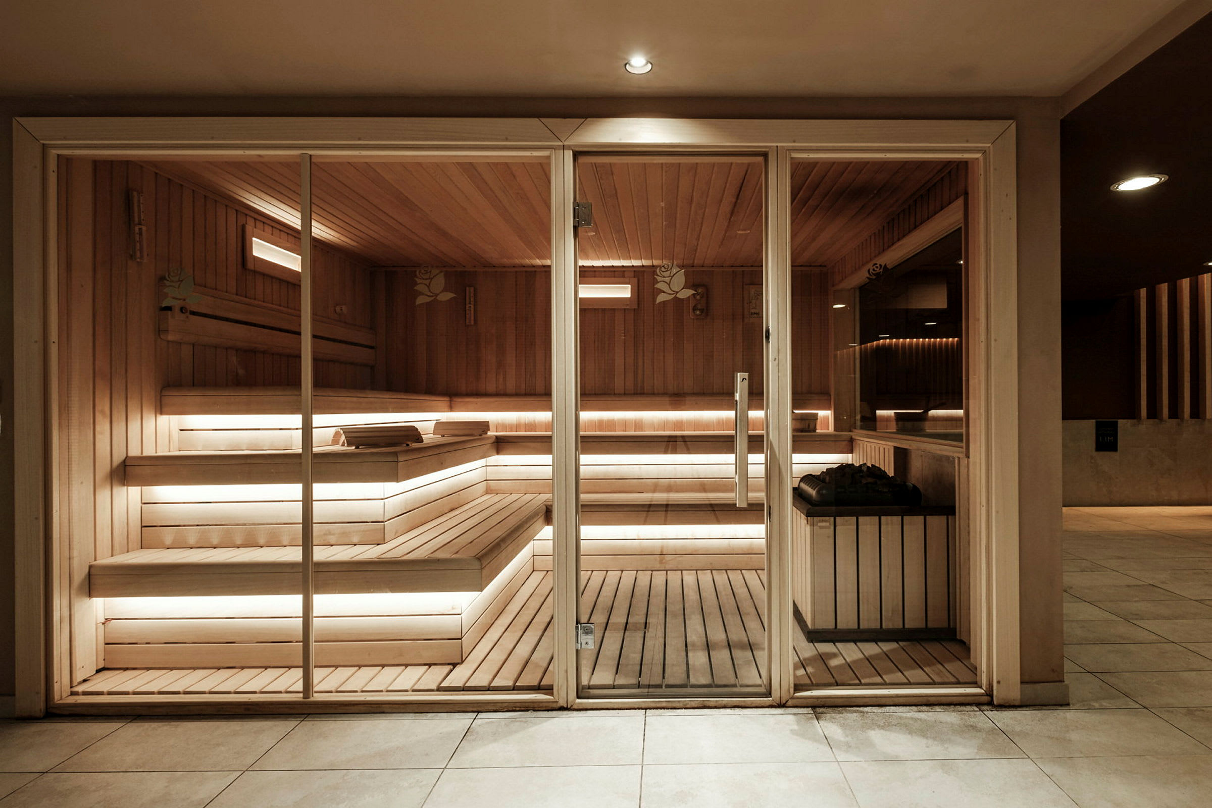 En sauna med træinteriør, glasdør og bænke samt belysning. (AI-genereret tekst)