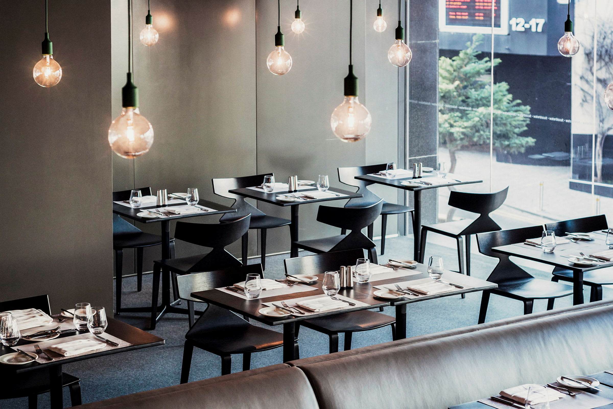 En moderne restaurant med elegant dækkede borde og hængende elpærer. (AI-genereret tekst)
