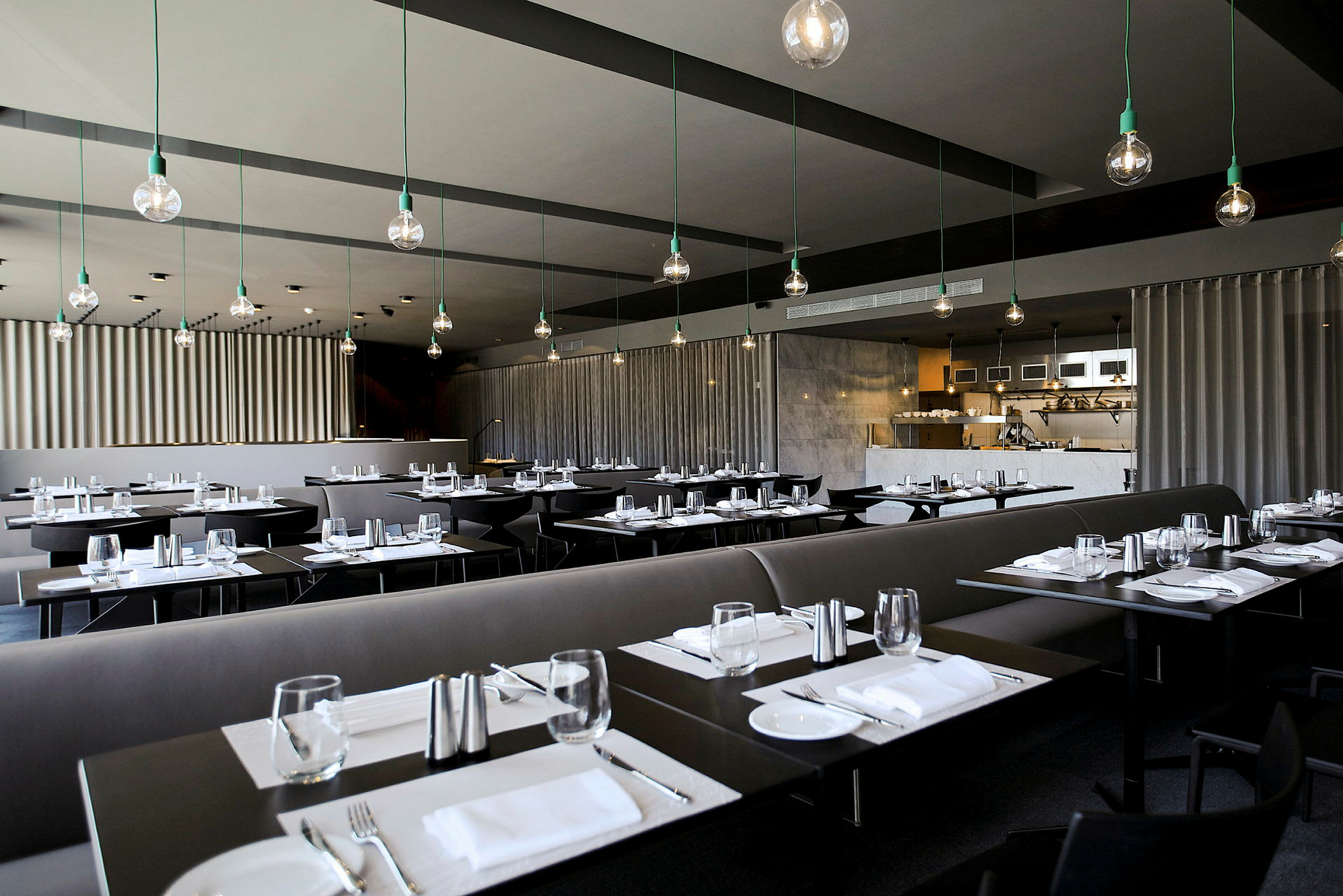 En moderne restaurant med mørke borde, dækket op til måltid og stilfuld loftbelysning. (AI-genereret tekst)