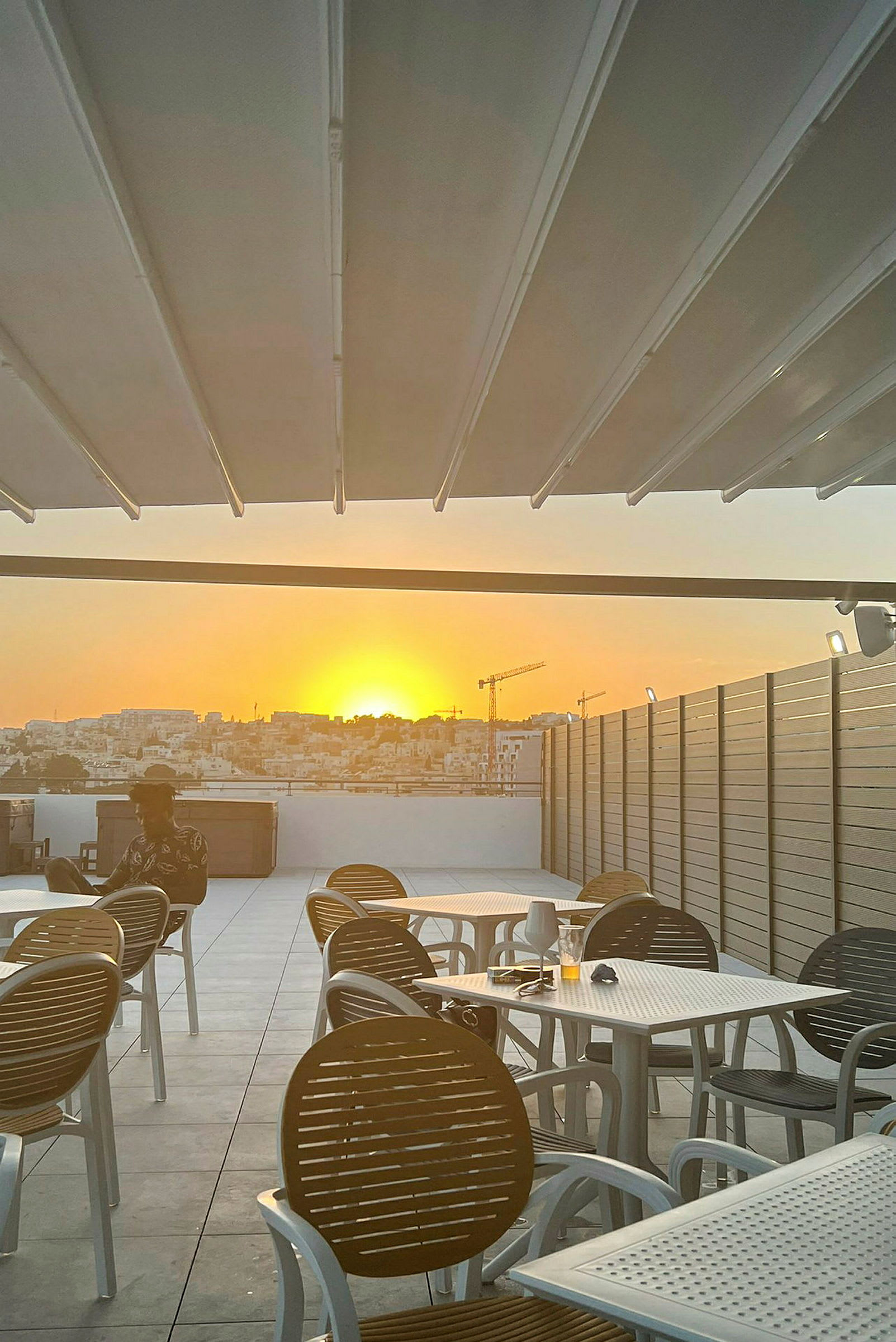 En terrasse med borde og stole, med solnedgangen i baggrunden. (AI-genereret tekst)