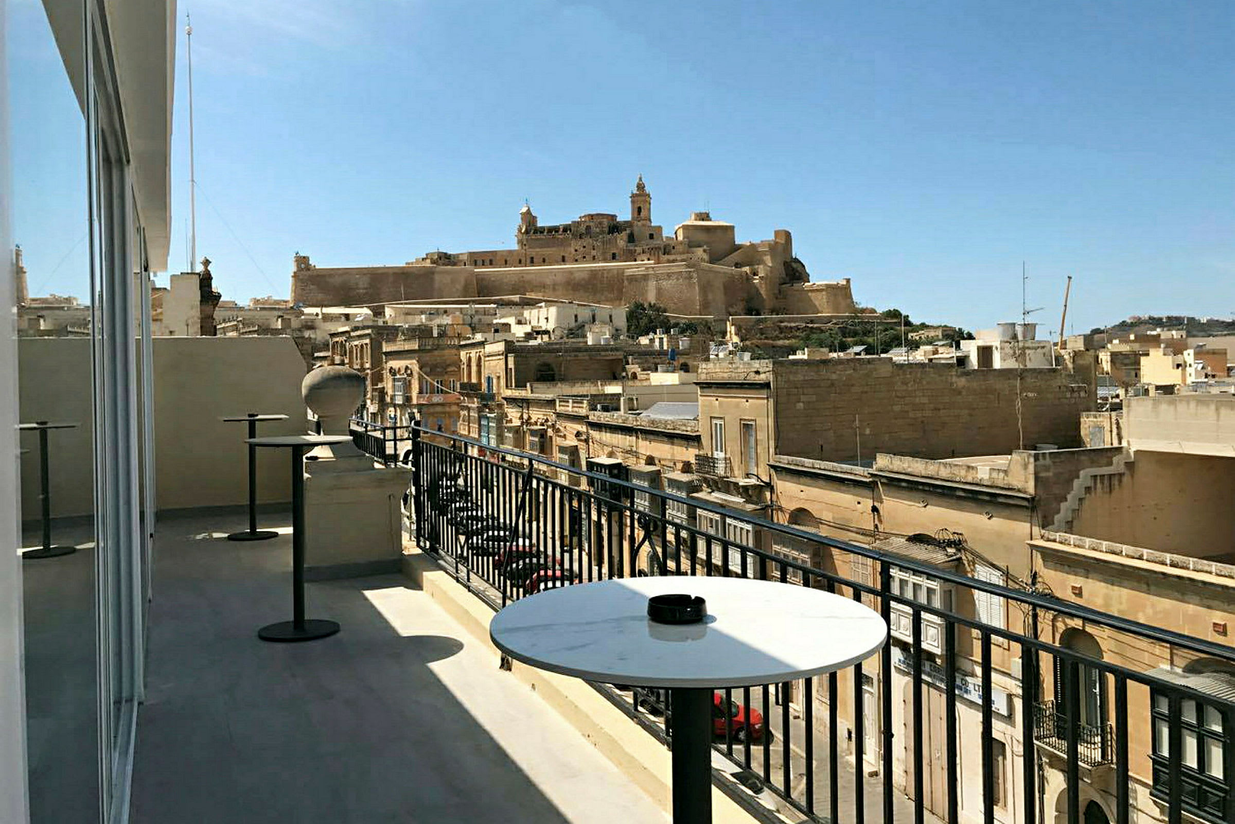 Udsigt fra en terrasse med borde over bygninger og en historisk fæstning på en bakke. (AI-genereret tekst)
