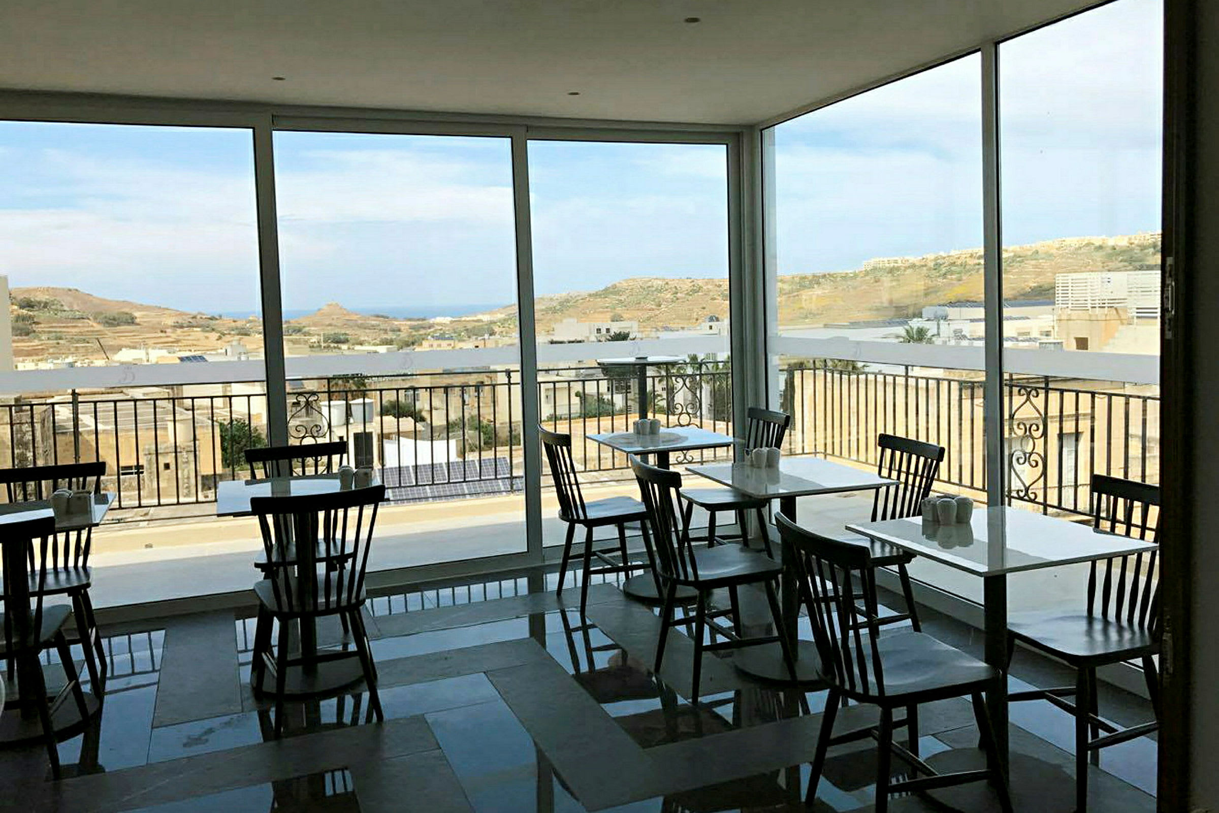 Et caféområde med store vinduer og udsigt til et landskab. (AI-genereret tekst)