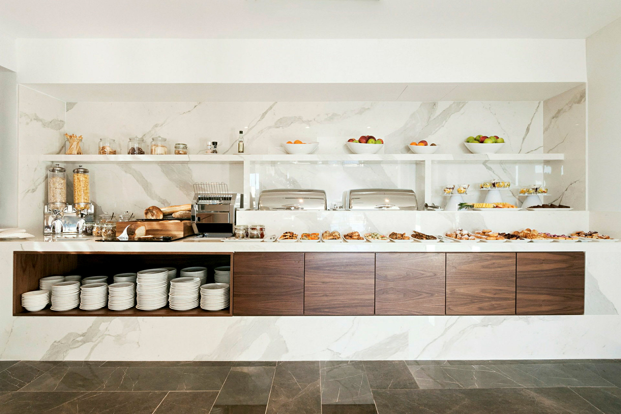 En buffet med forskellige morgenmadsvalg arrangeret på en moderne og stilfuld bænk med marmordetaljer. (AI-genereret tekst)