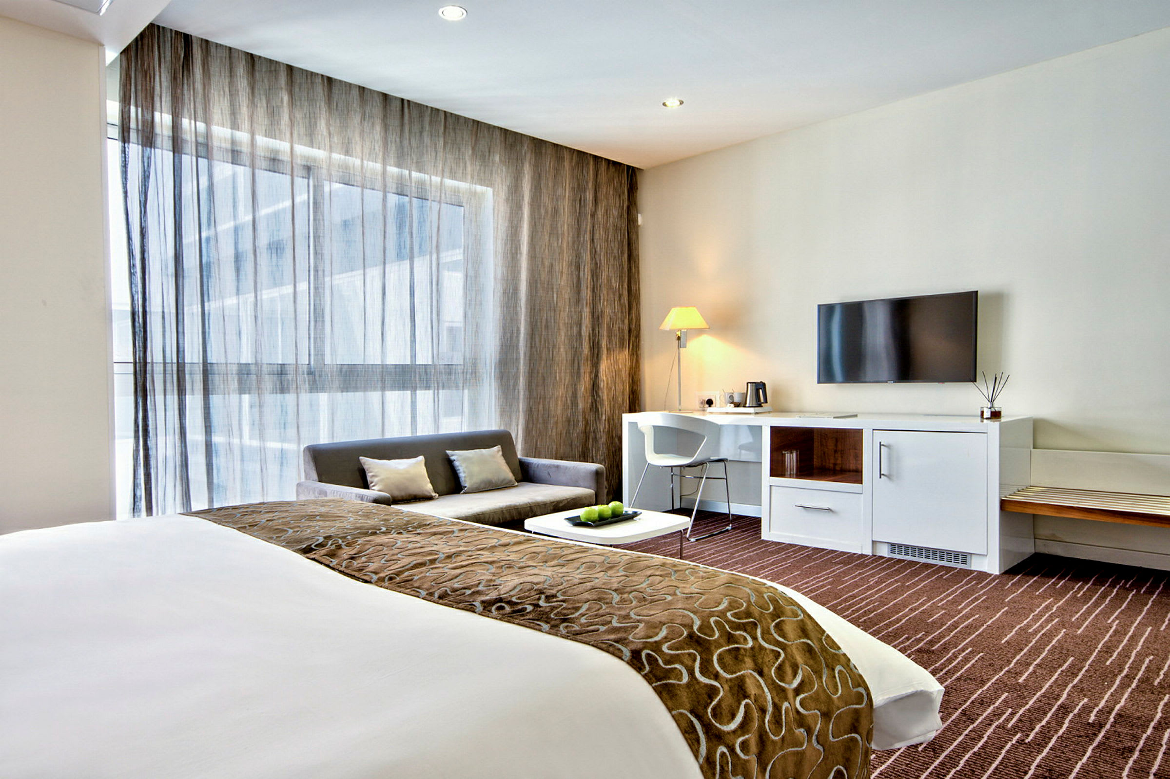 Et moderne hotelværelse med seng, sofa, skrivebord og TV. (AI-genereret tekst)
