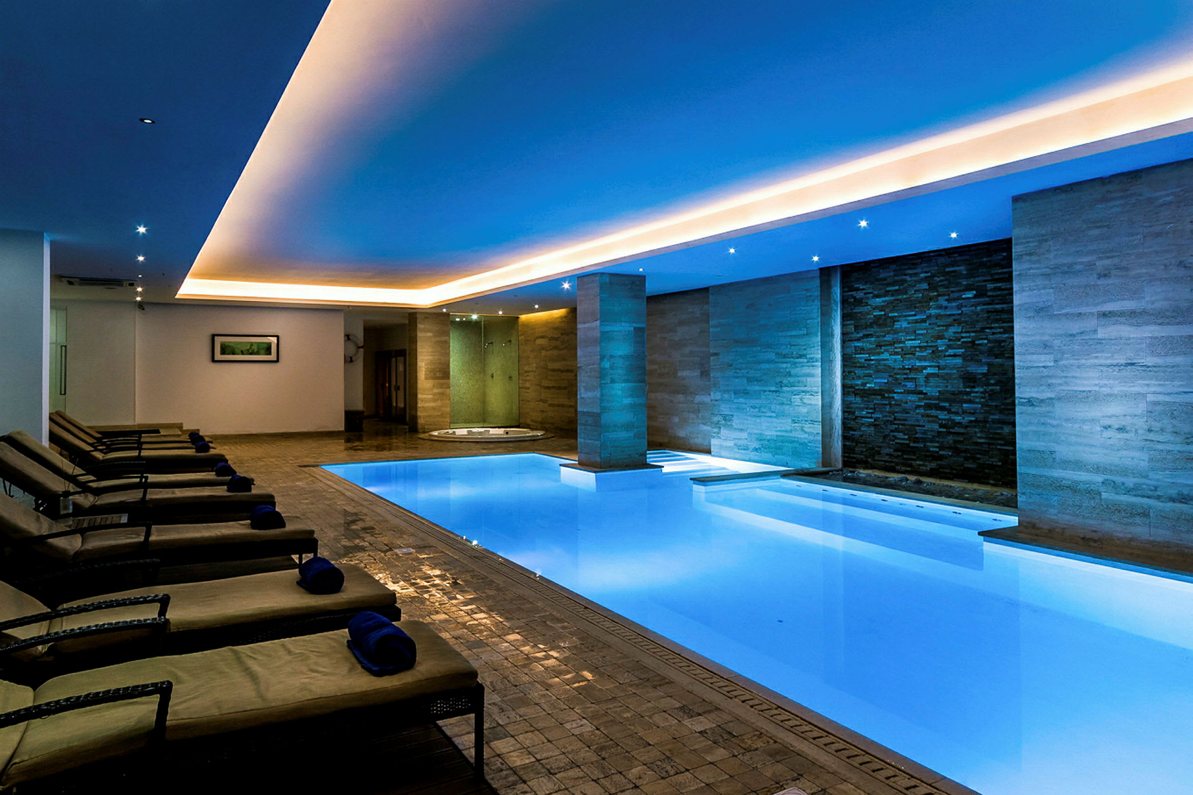 Billede af et moderne indendørs spa med oplyst swimmingpool, liggestole og afslappende atmosfære. (AI-genereret tekst)