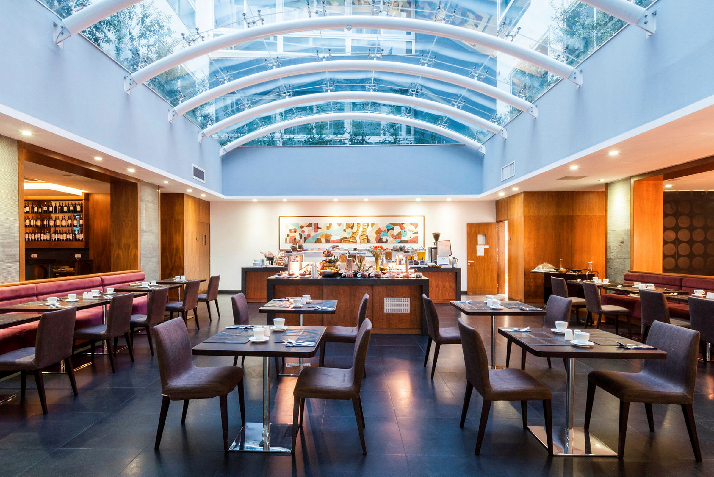 Restaurant med elegant interiør, borde og stole samt en gennemsigtig tagkonstruktion. (AI-genereret tekst)