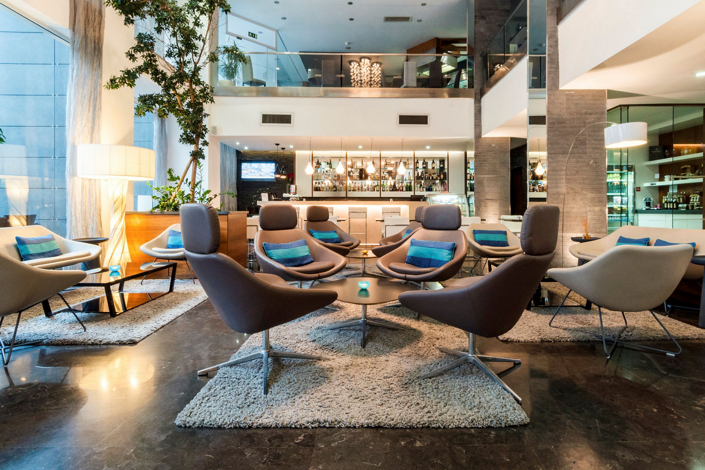 En hotellobby med moderne møbler, flere sofaer og lænestole med puder i et stilrent miljø. En bar ses i baggrunden. (AI-genereret tekst)