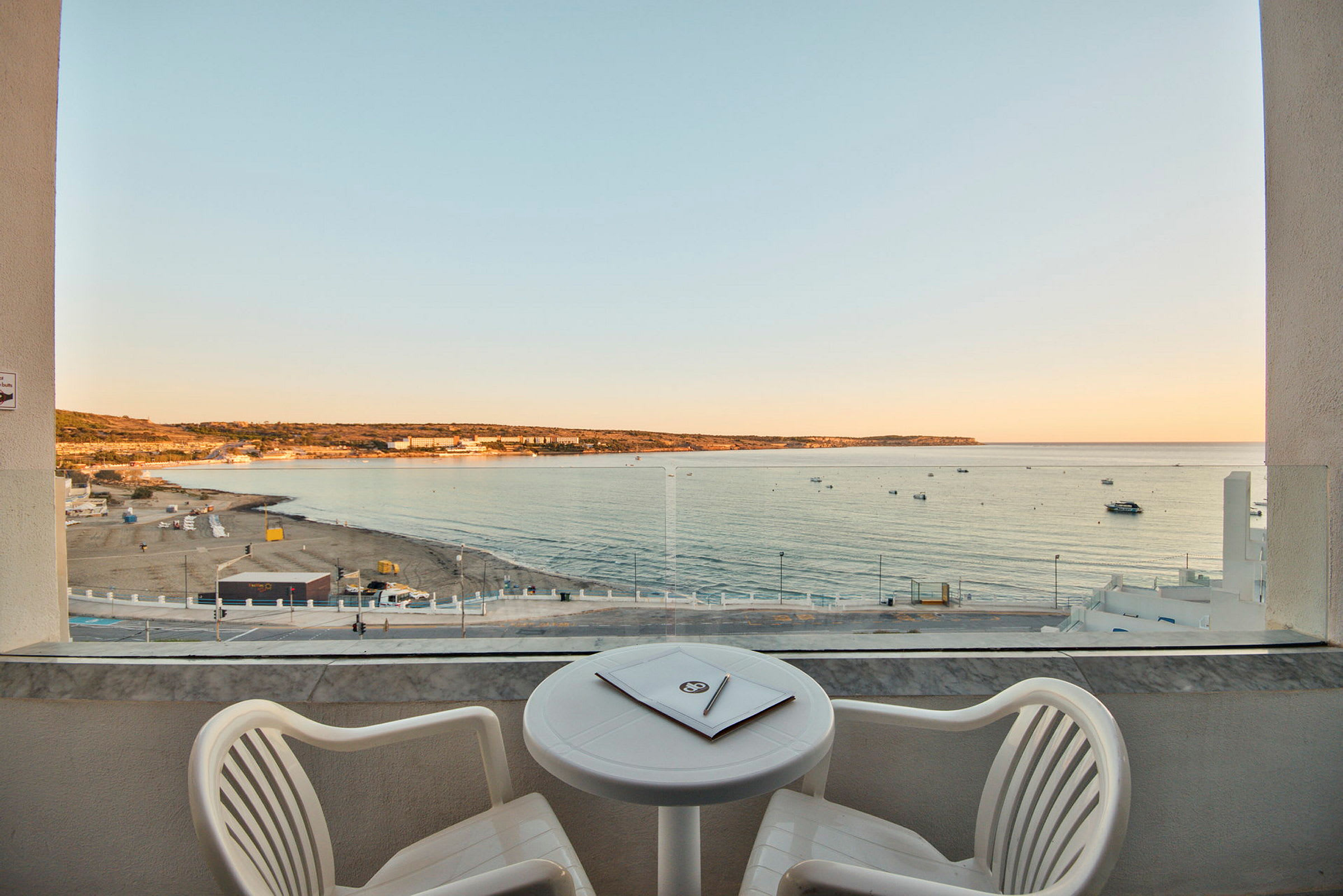 Udsigt fra en balkon over en sandstrand og havet ved solnedgang. (AI-genereret tekst)