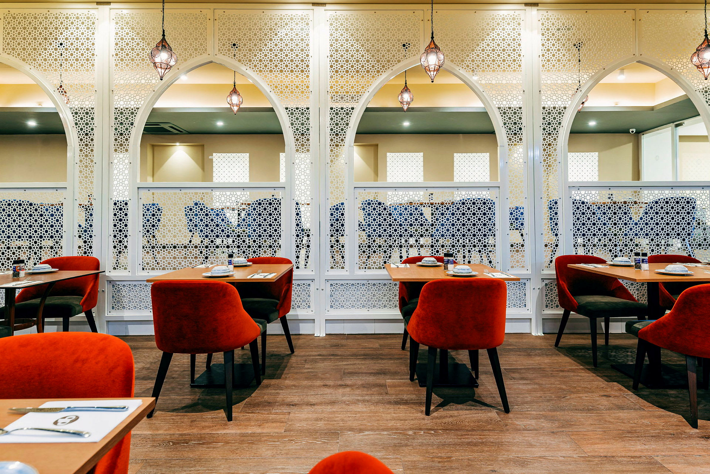 Et indrettet restaurantområde med røde stole og træborde, omgivet af hvid dekoration. (AI-genereret tekst)