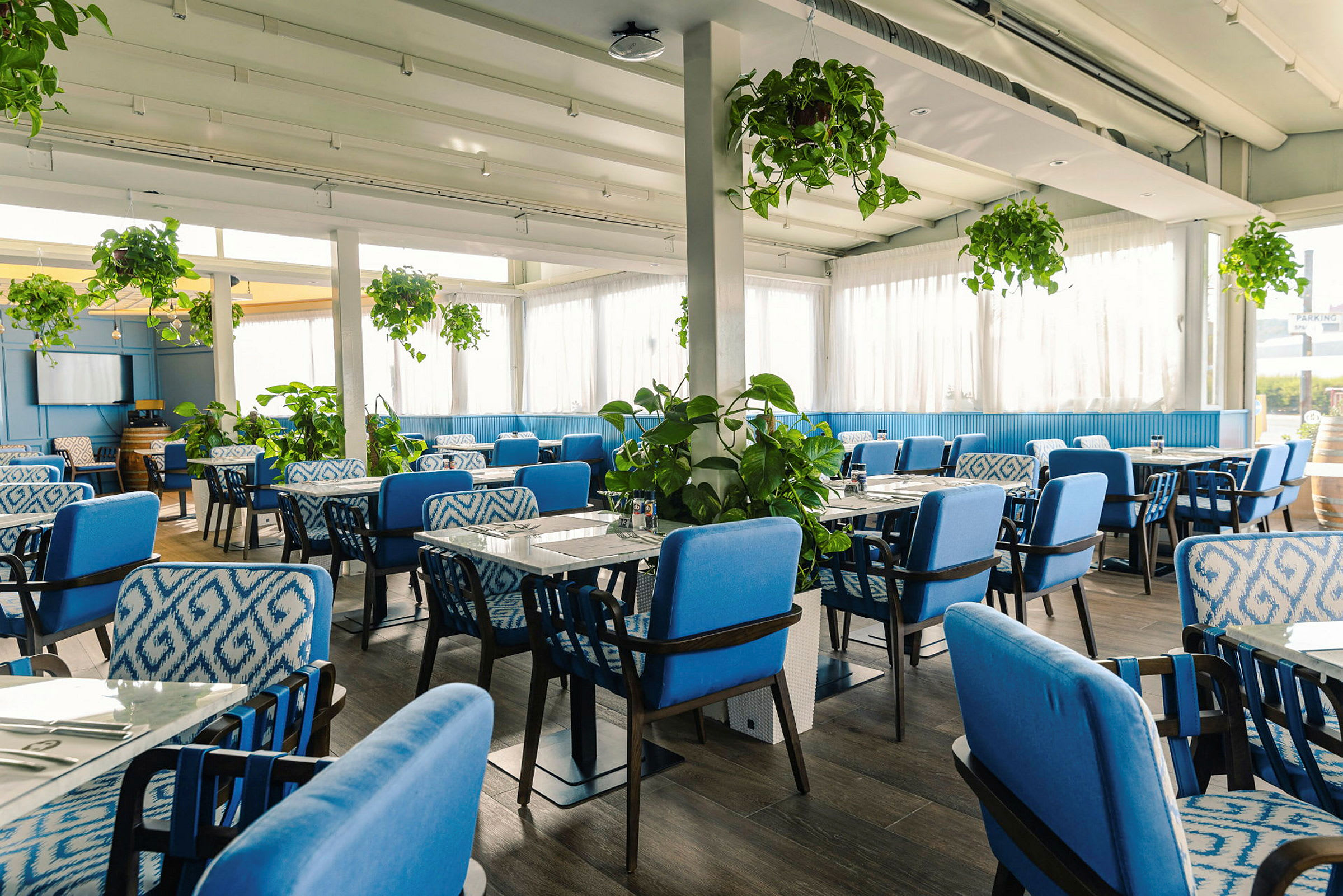 En restaurantinteriør med blå stole og grønne planter. (AI-genereret tekst)