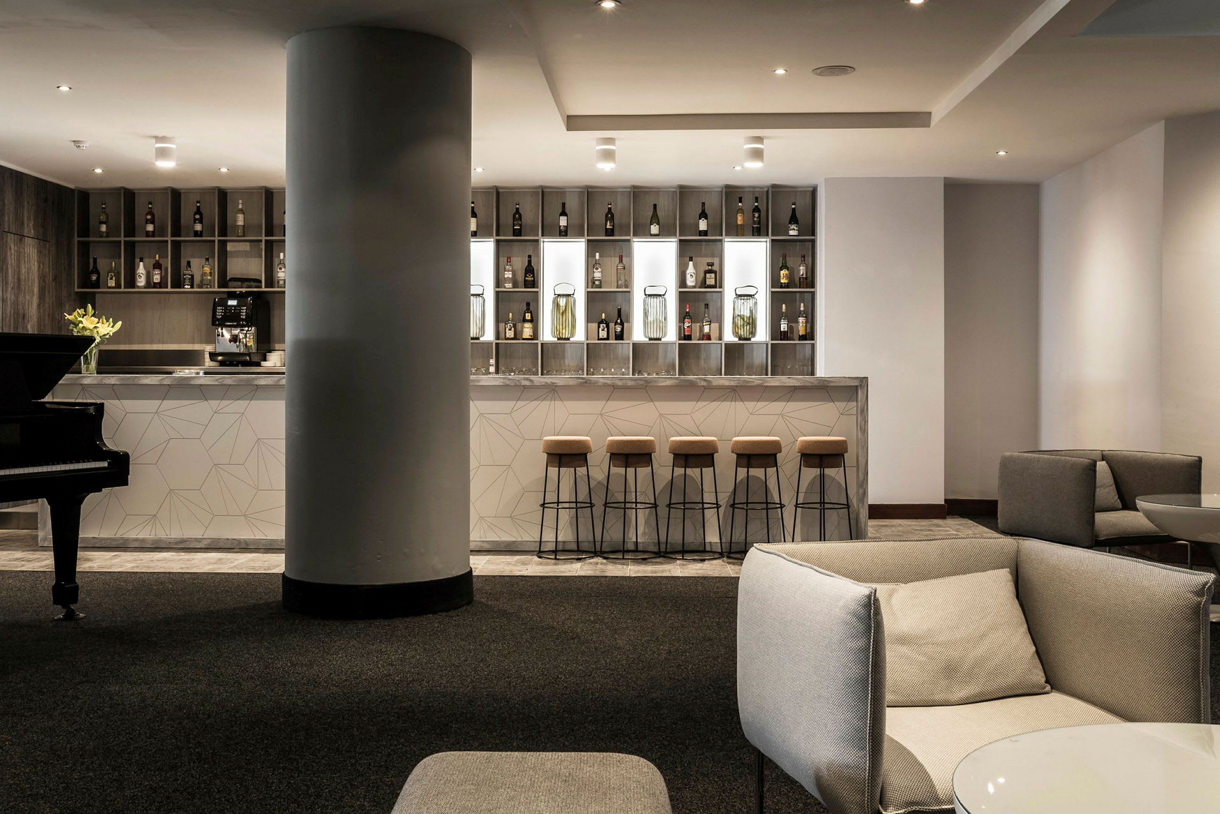 En moderne hotelbar med høje barstole og et stilfuldt design. Til venstre ses et klaver. (AI-genereret tekst)