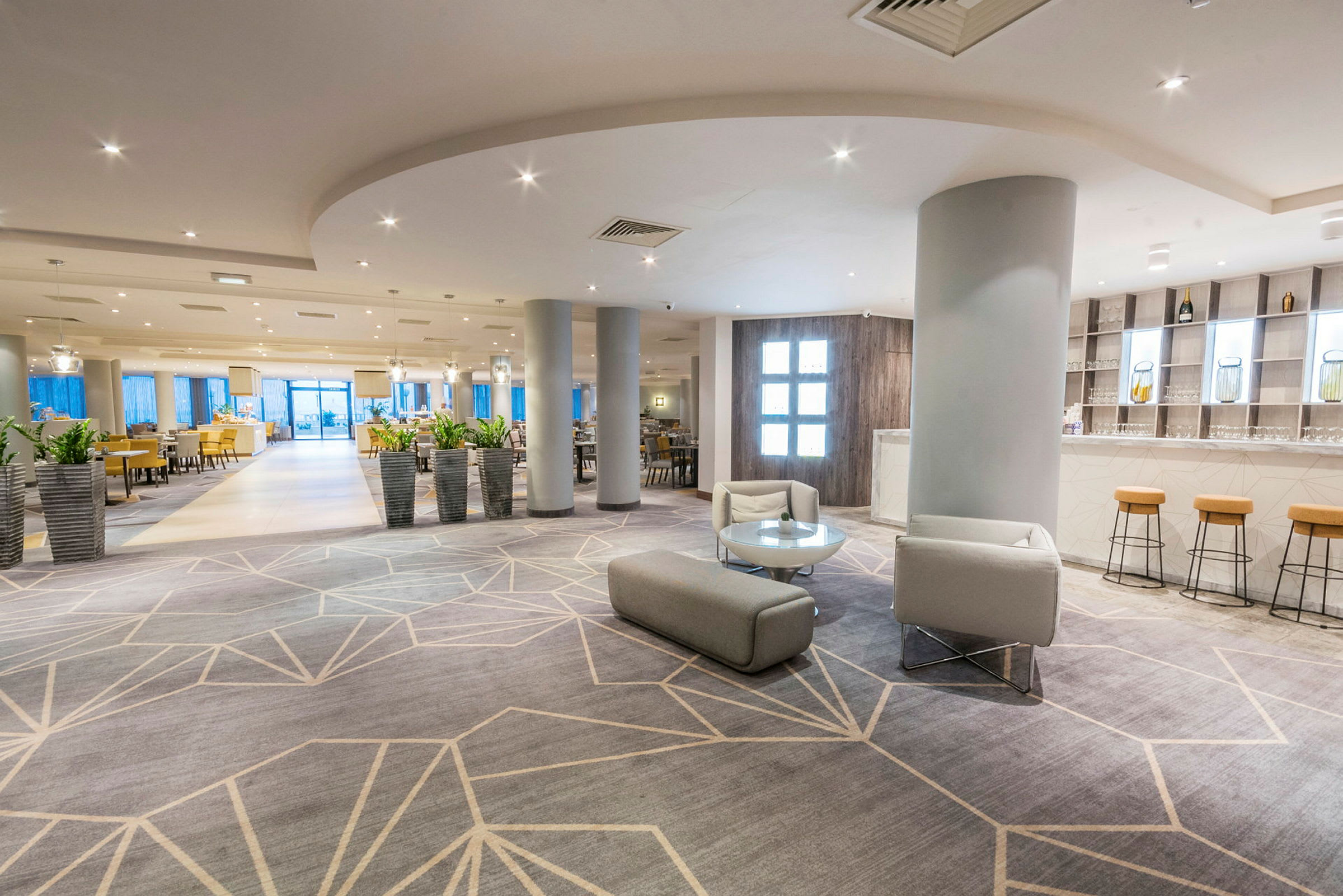 En lys og moderne hotellobby med siddepladser og flere planter i krukker. (AI-genereret tekst)