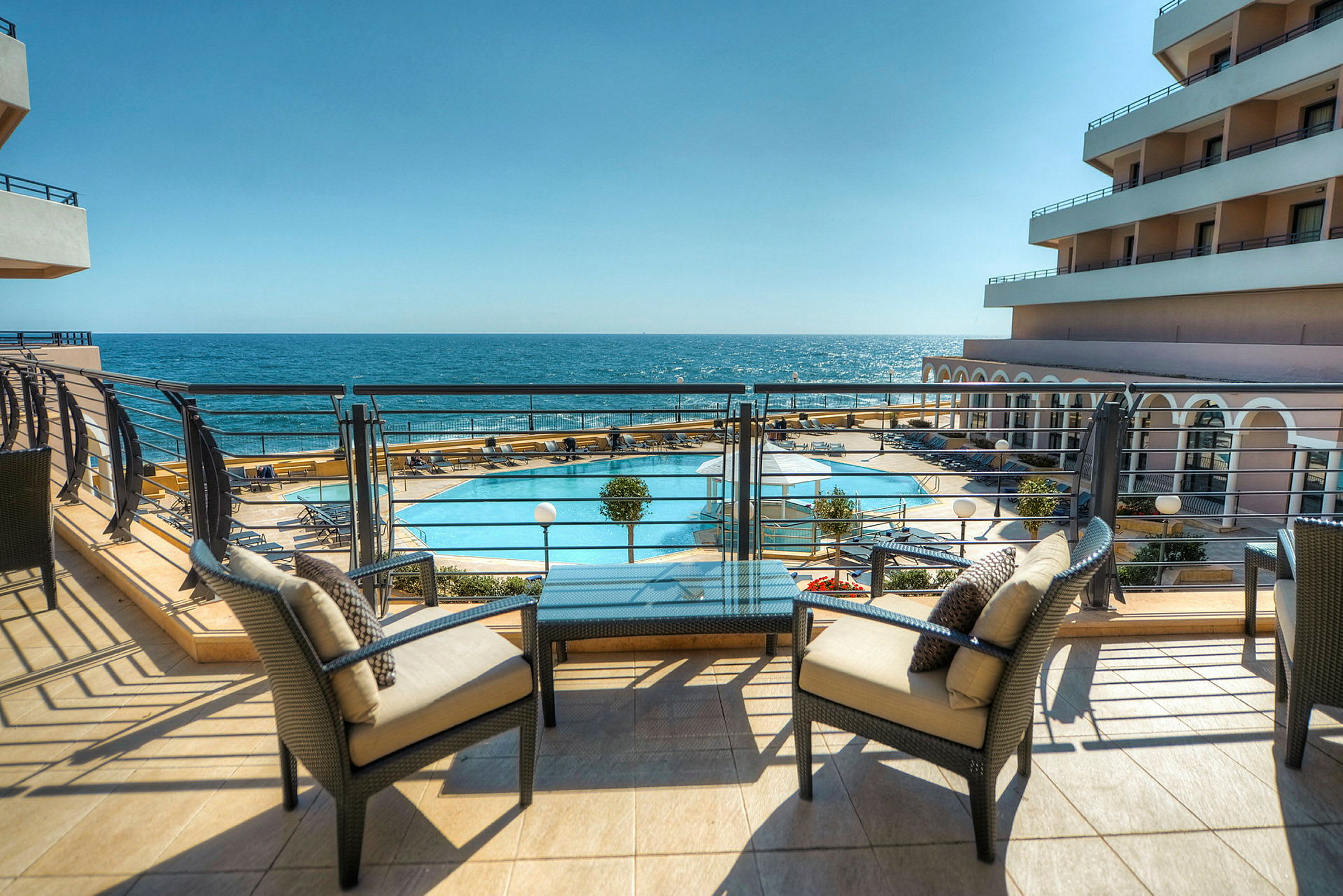 Terrasse med udsigt over en pool og havet i baggrunden. (AI-genereret tekst)