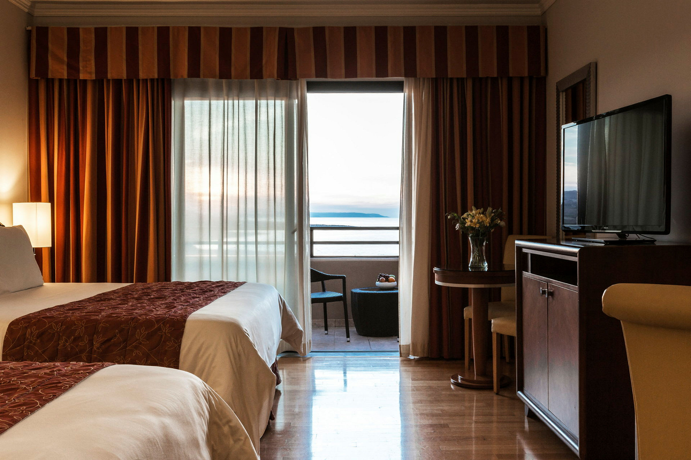 Et hotelværelse med to senge, en balkon med udsigt over havet, og et mindre bord med stole. (AI-genereret tekst)