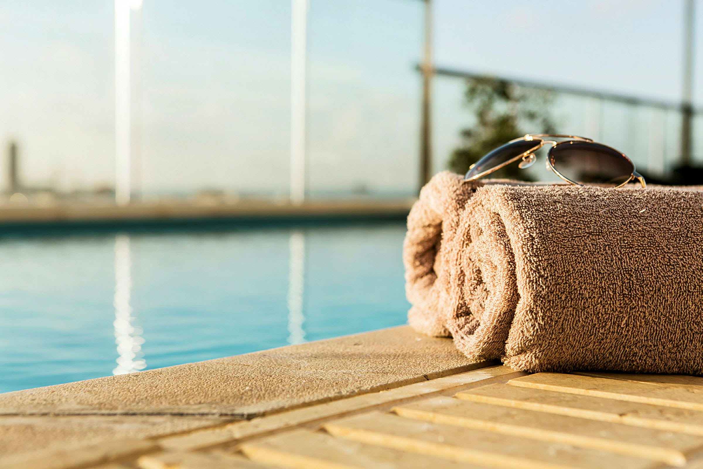 Et sammenrullet håndklæde med et par solbriller placeret ovenpå ved kanten af en pool. (AI-genereret tekst)