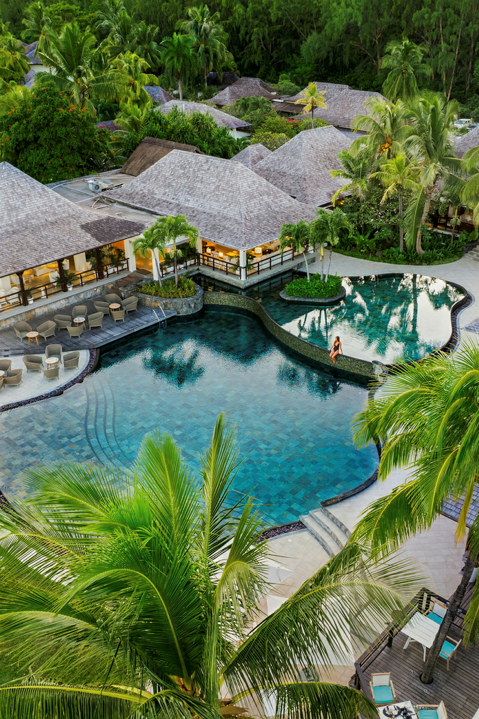 En swimmingpool ved en resort omgivet af tropiske planter og palmer. (AI-genereret tekst)