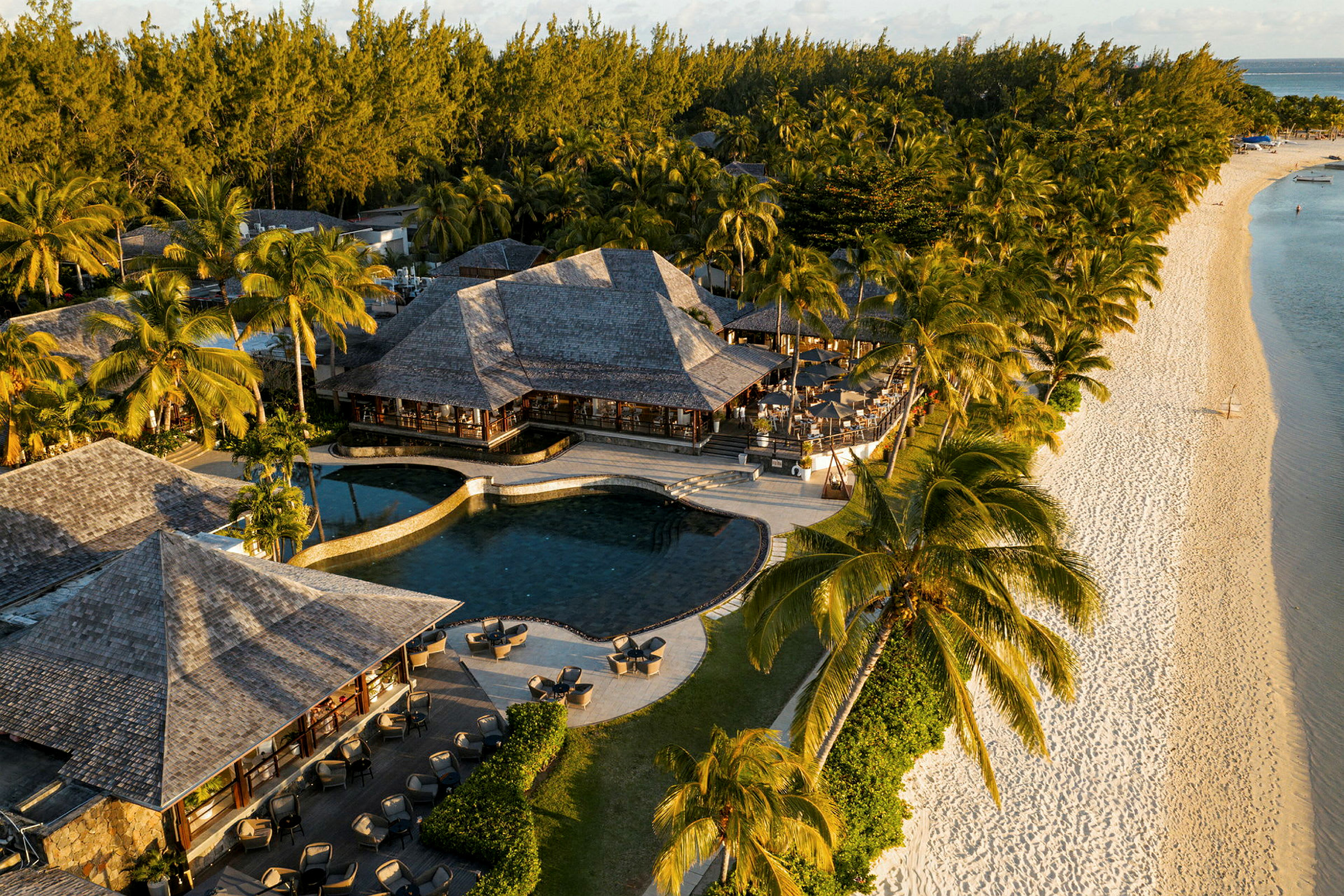 Luftfoto af en resort ved en strand med pools, bygninger og omgivende palmetræer. (AI-genereret tekst)