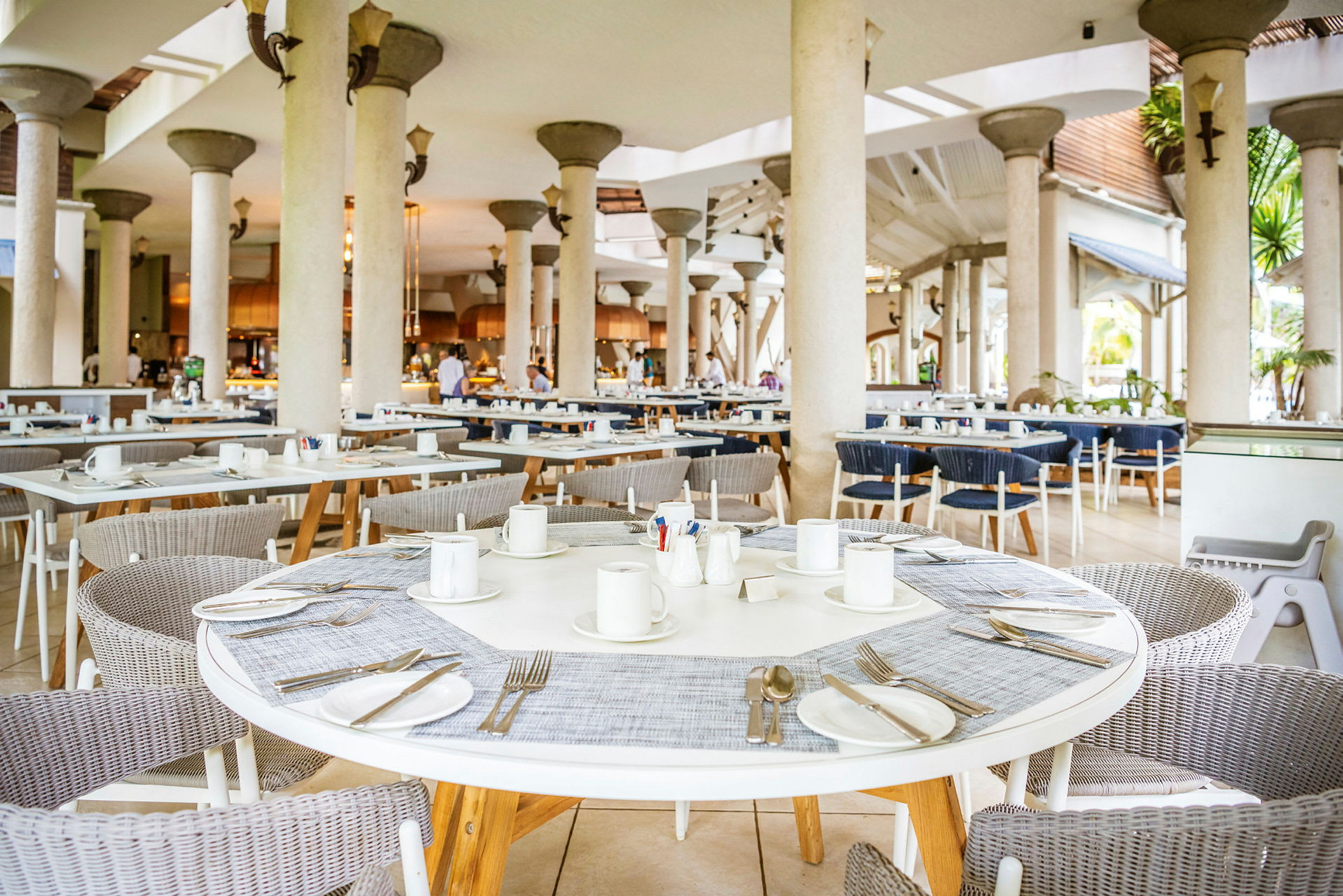 Et luftigt restaurantområde med runde borde, stole og dækkede pladser. (AI-genereret tekst)