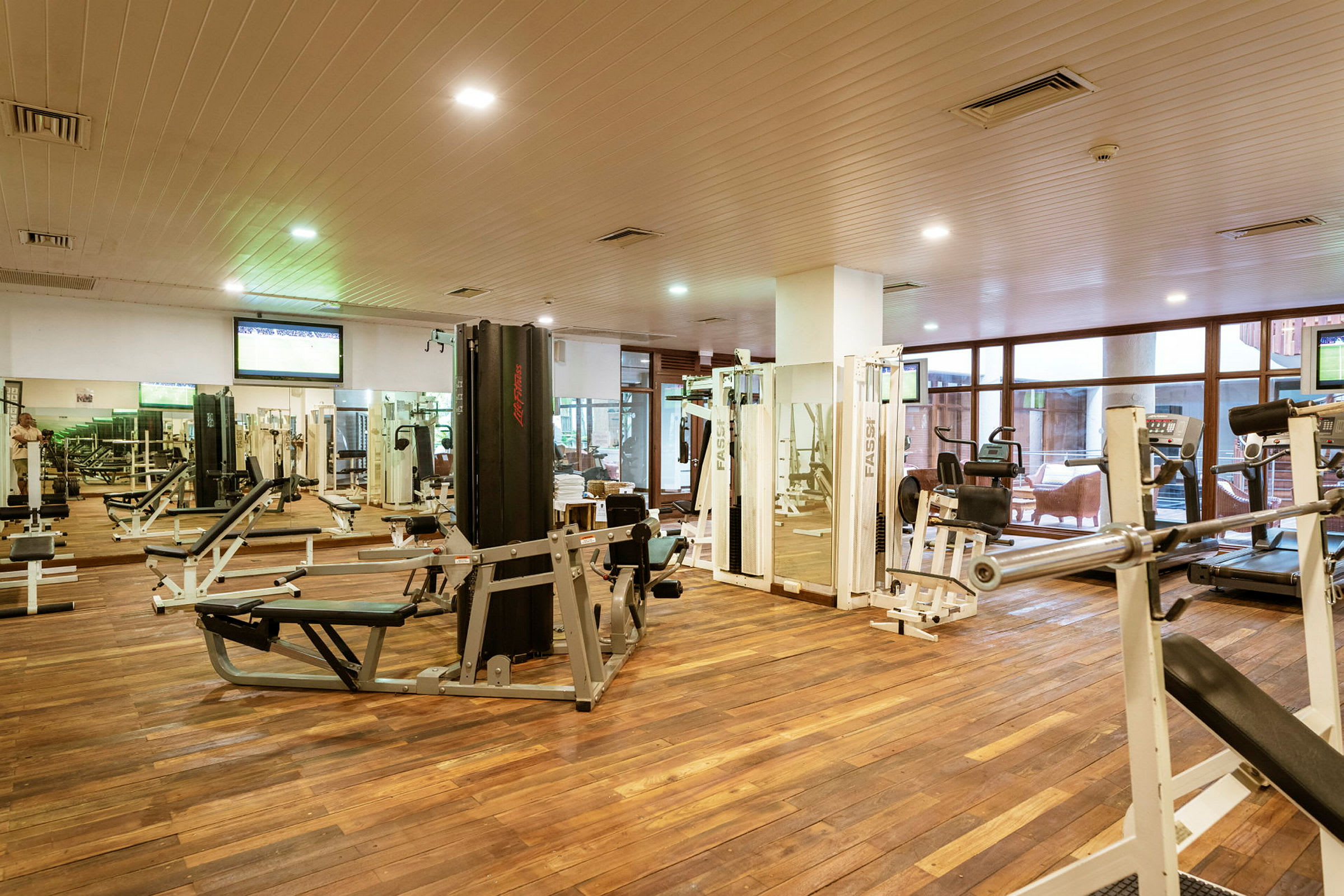 Et fitnesscenter med træningsmaskiner og vægte, beliggende i et rum med trægulv. (AI-genereret tekst)