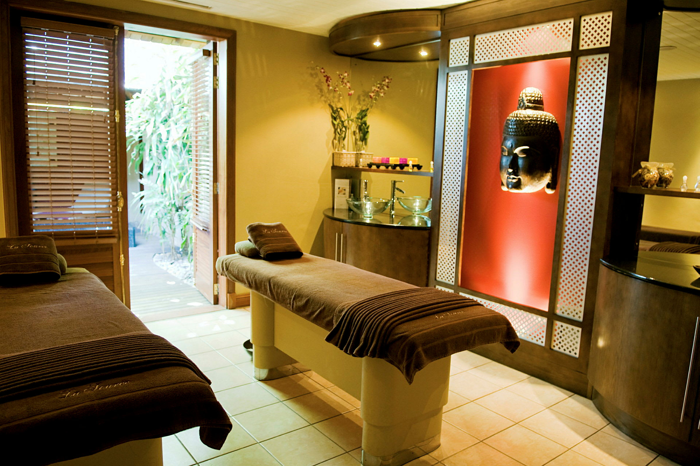 Et spa-rum med massagebænke, Buddha-dekoration og åben dør til haven. (AI-genereret tekst)