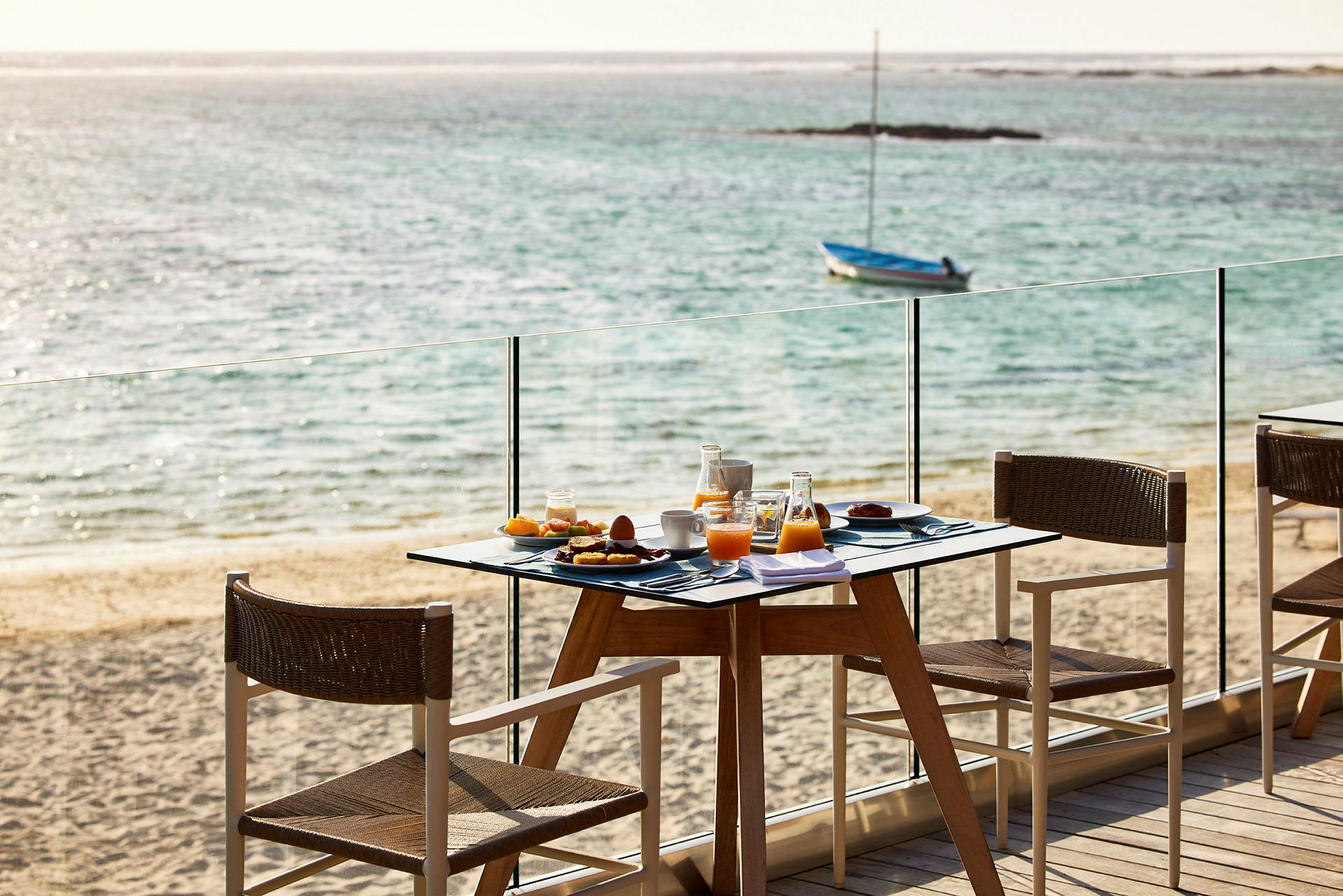 En morgenmad serveres ved et bord nær stranden med havet i baggrunden. (AI-genereret tekst)