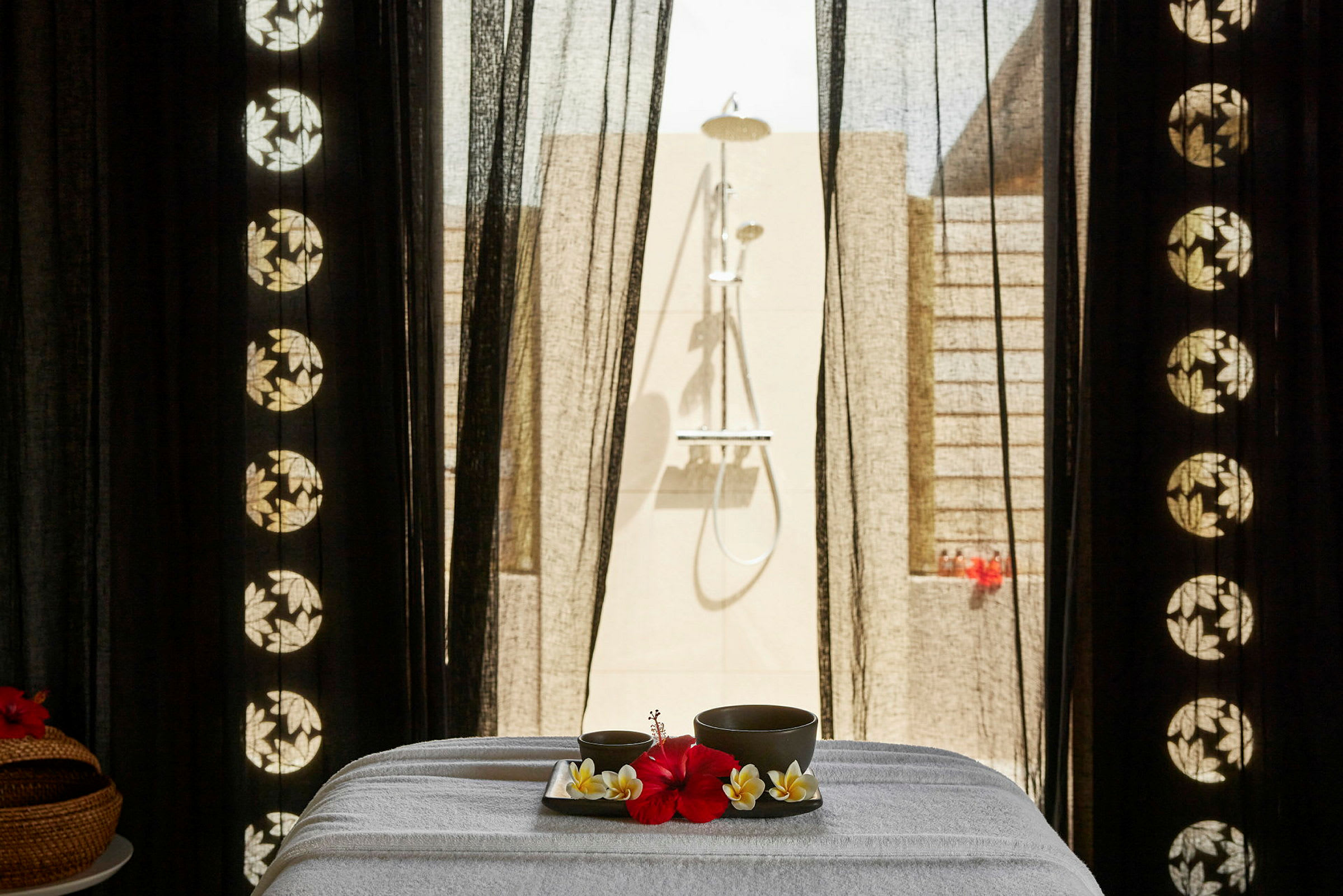 Et spa-bord med en bakke indeholdende en rød blomst og drikkekopper, placeret foran en udendørs bruser. (AI-genereret tekst)