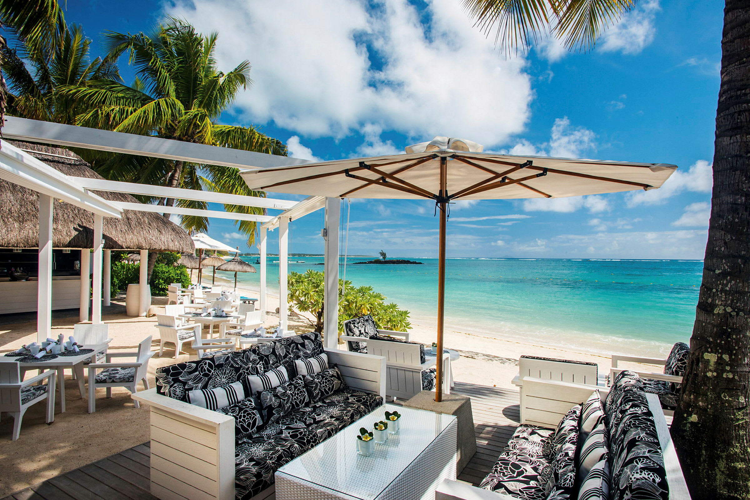 Restaurantområde ved stranden med siddepladser, parasoller og udsigt over havet. (AI-genereret tekst)