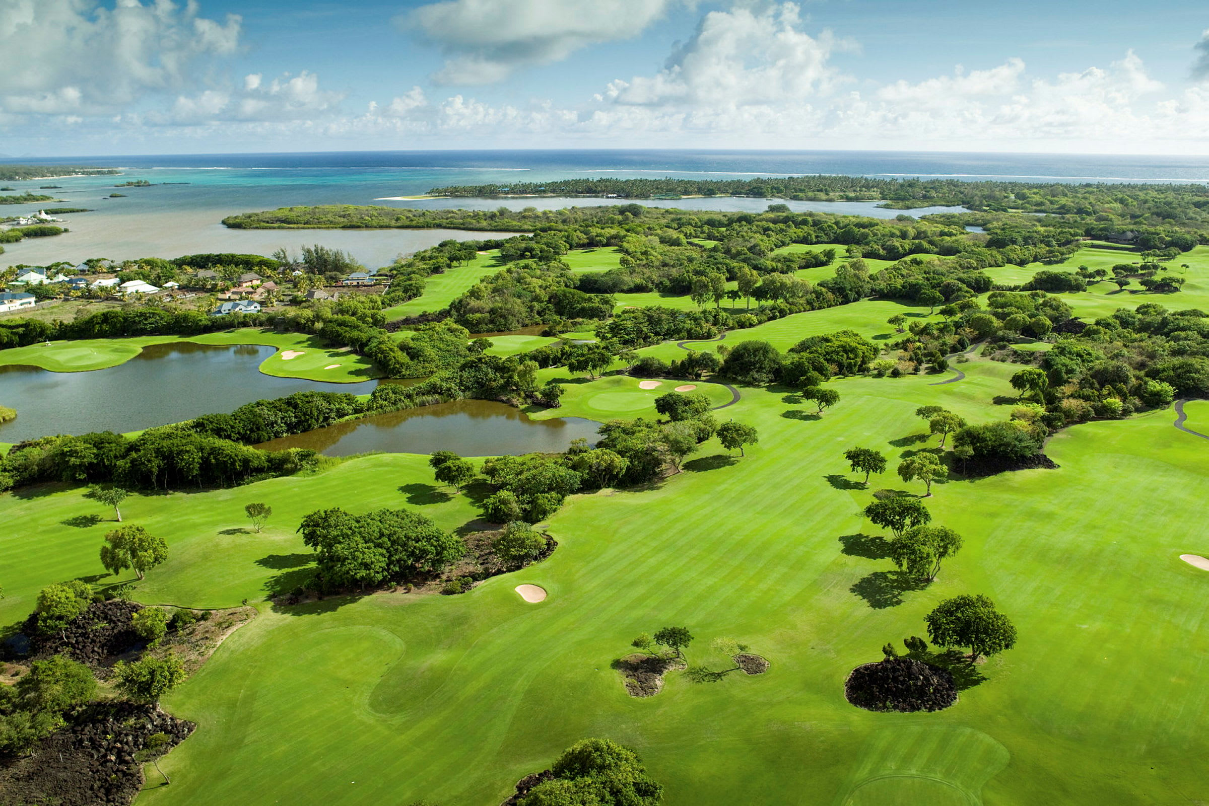 Luftfoto af en golfbane omgivet af grønt med havet i baggrunden. (AI-genereret tekst)
